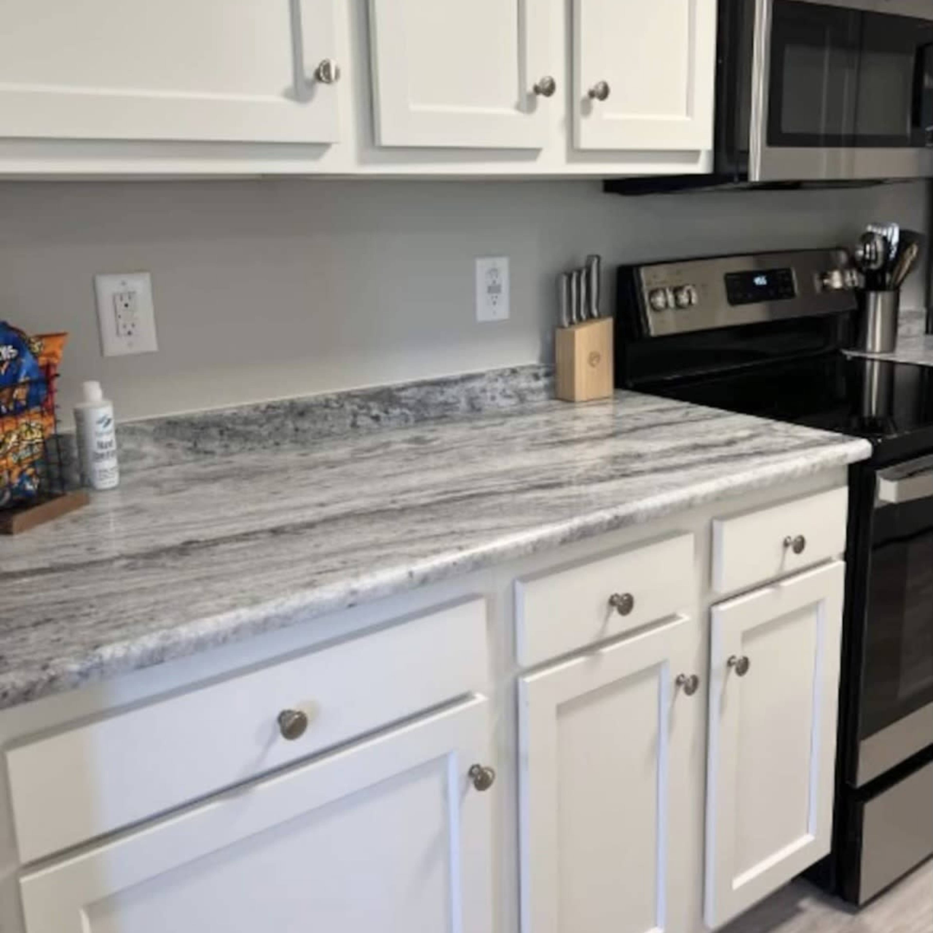 A kitchen countertop made of gray granite with white cabinets above and a black stove beneath a microwave.