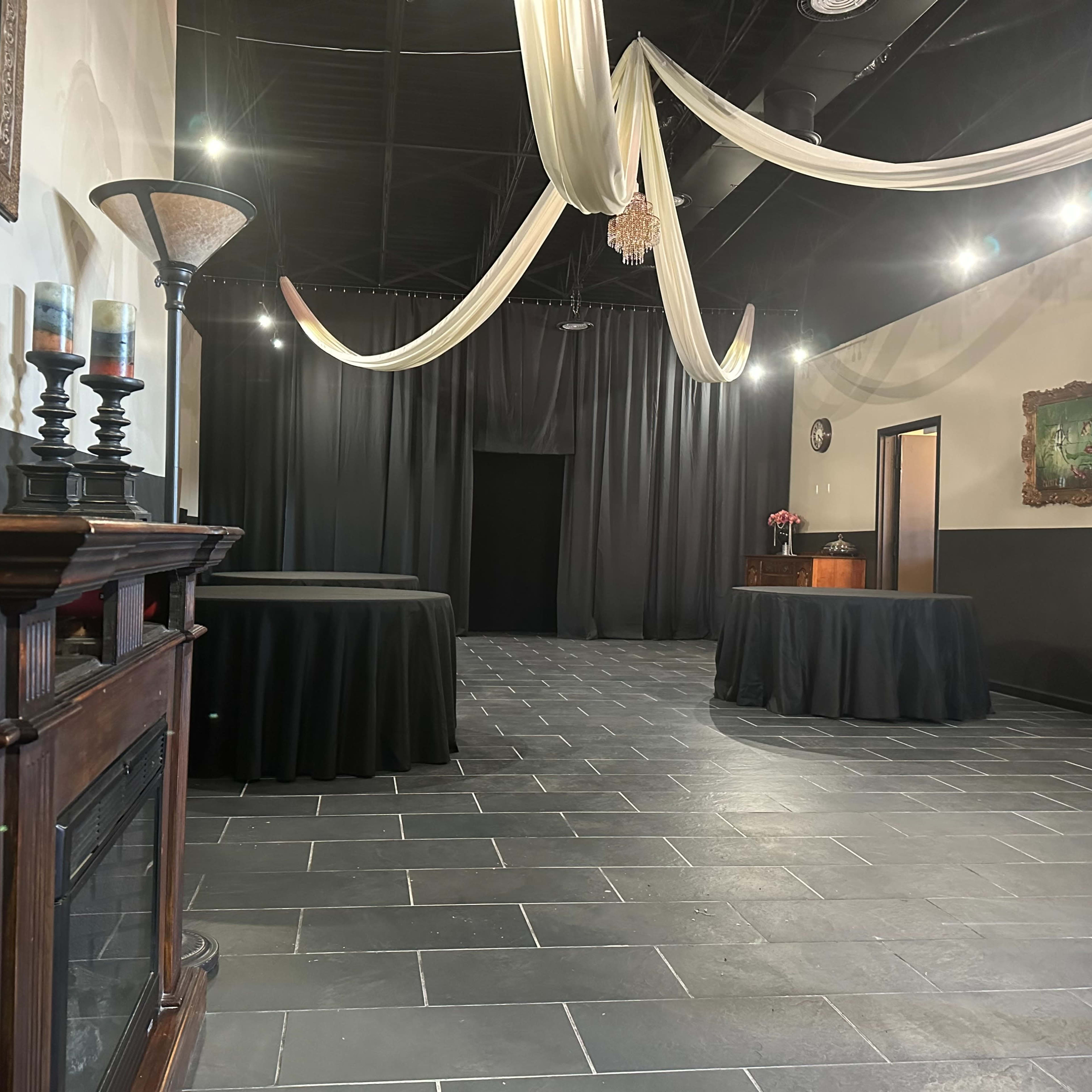 A dimly lit event space with black tablecloths, elegant décor, and a large draped fabric overhead.
