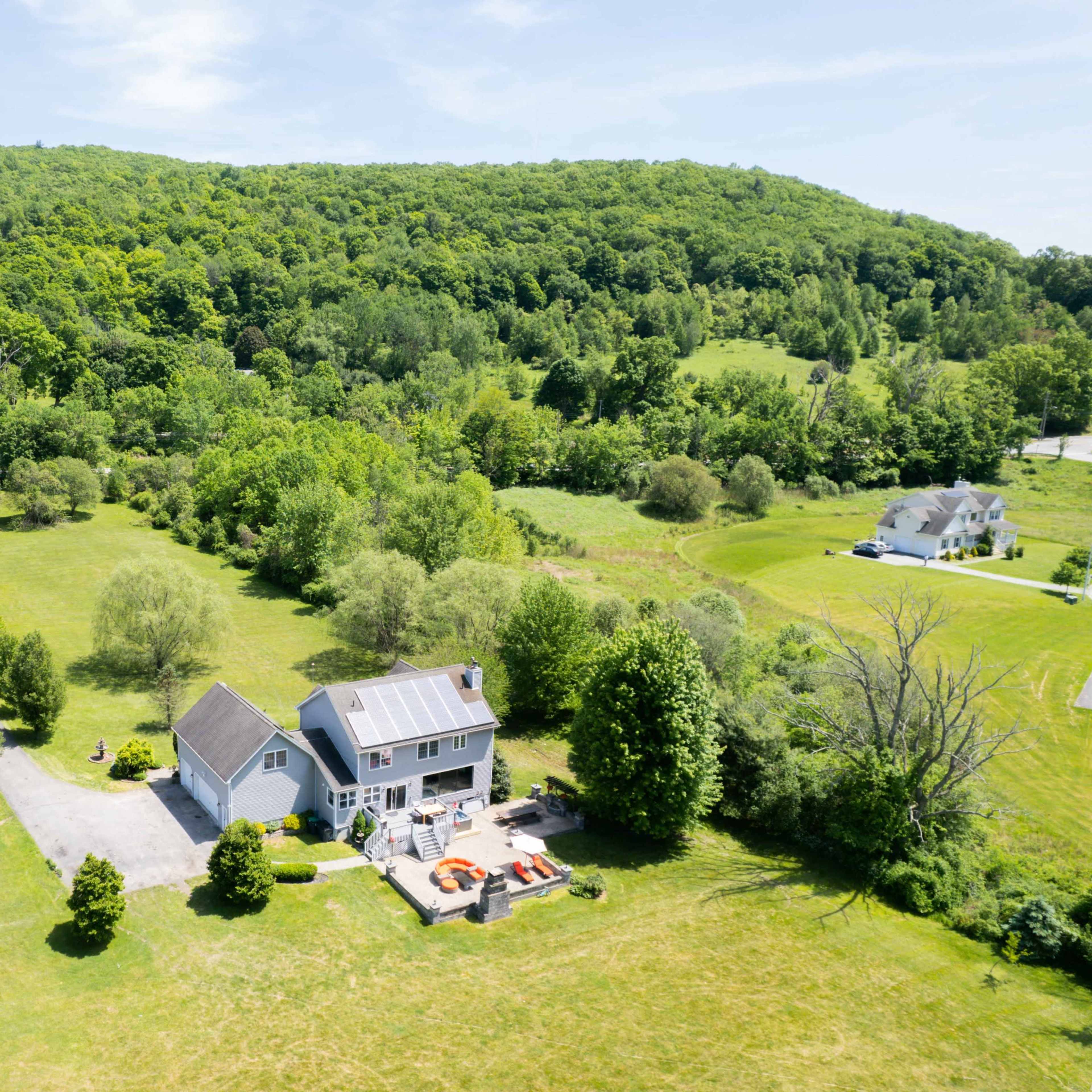 A spacious house with a large yard is surrounded by trees and hills in a rural landscape.