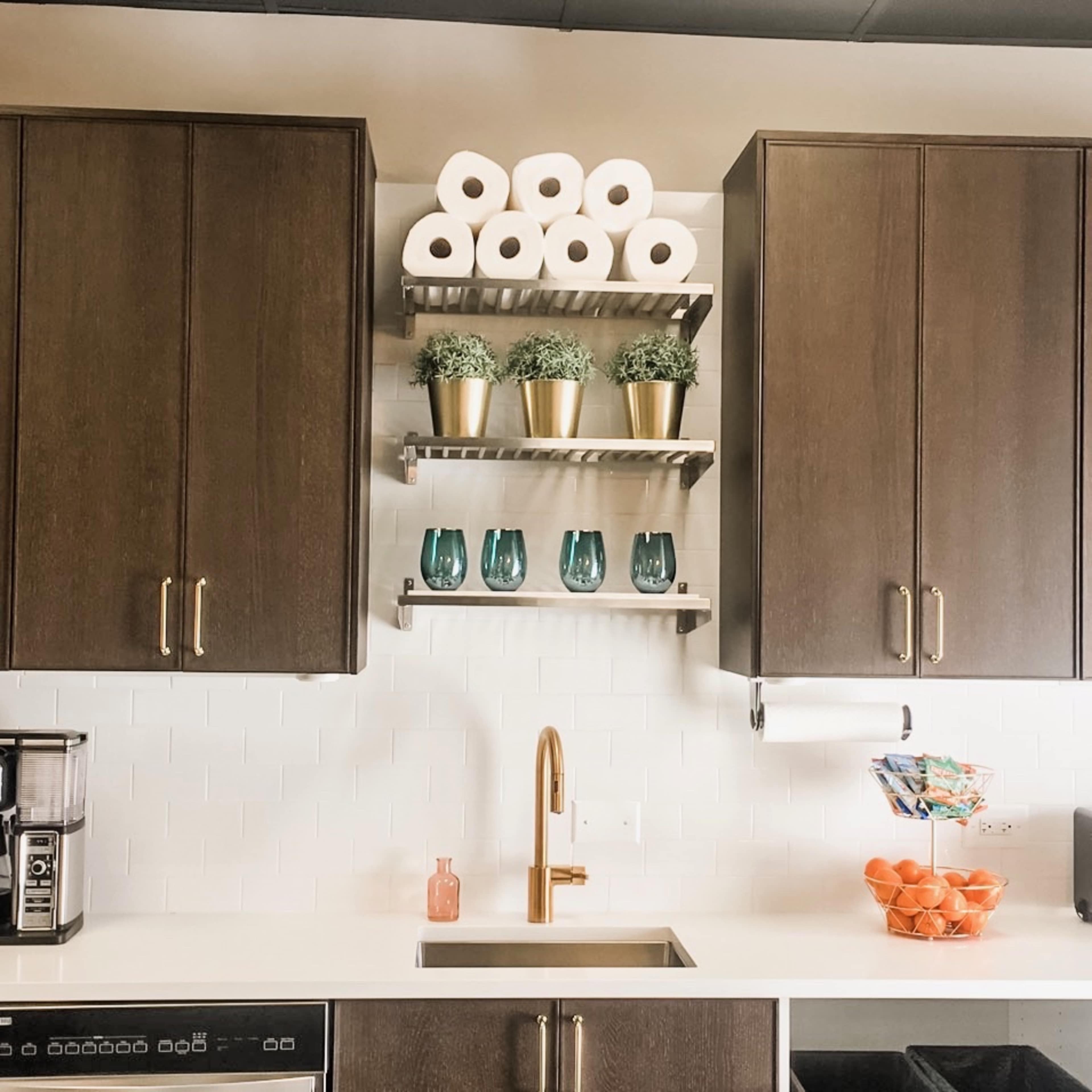 A modern kitchen with dark cabinetry, a metal shelf holding potted plants and blue glasses, and a coffee maker on the counter.