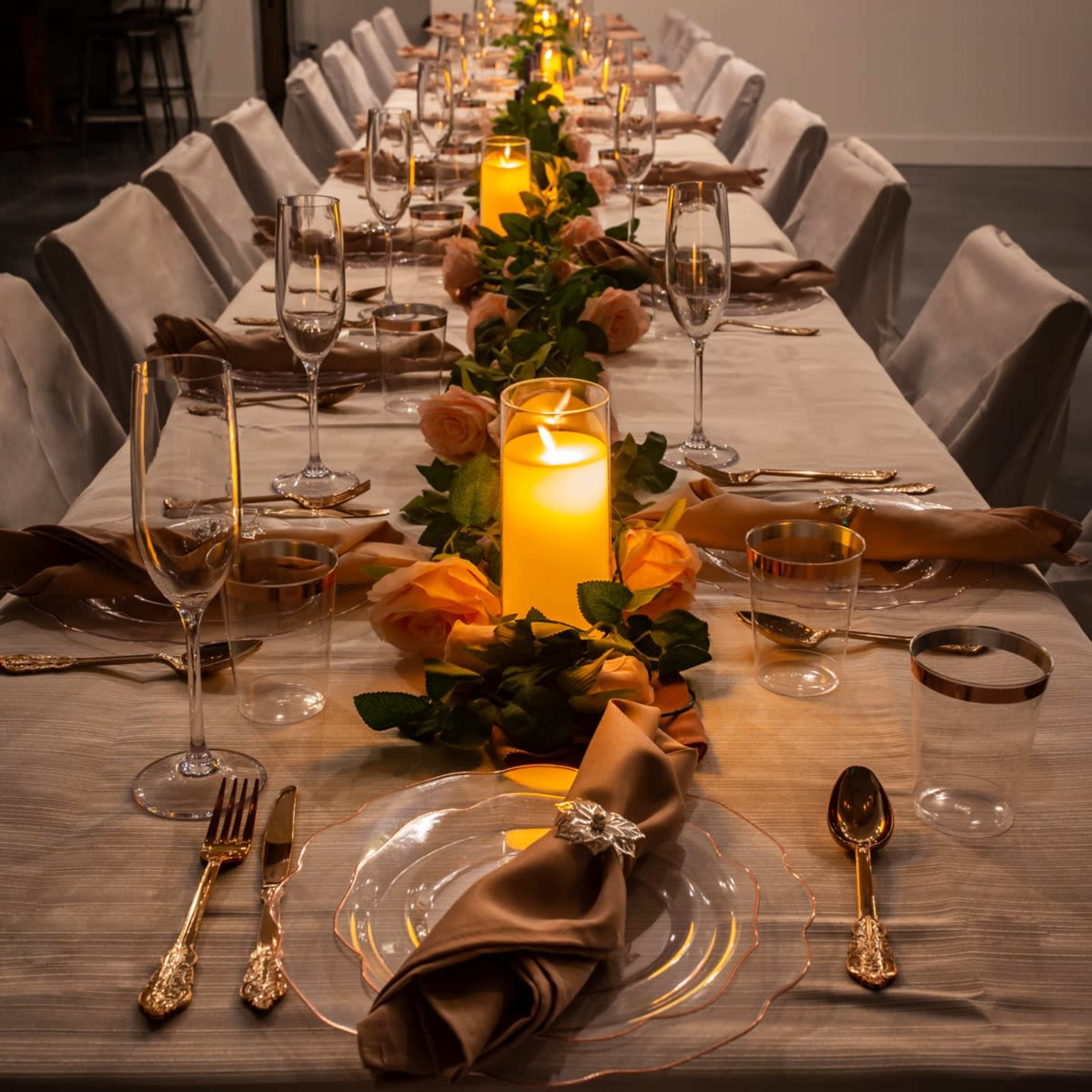 A long dining table is set for a formal event with elegant tableware, candles, and floral decorations.