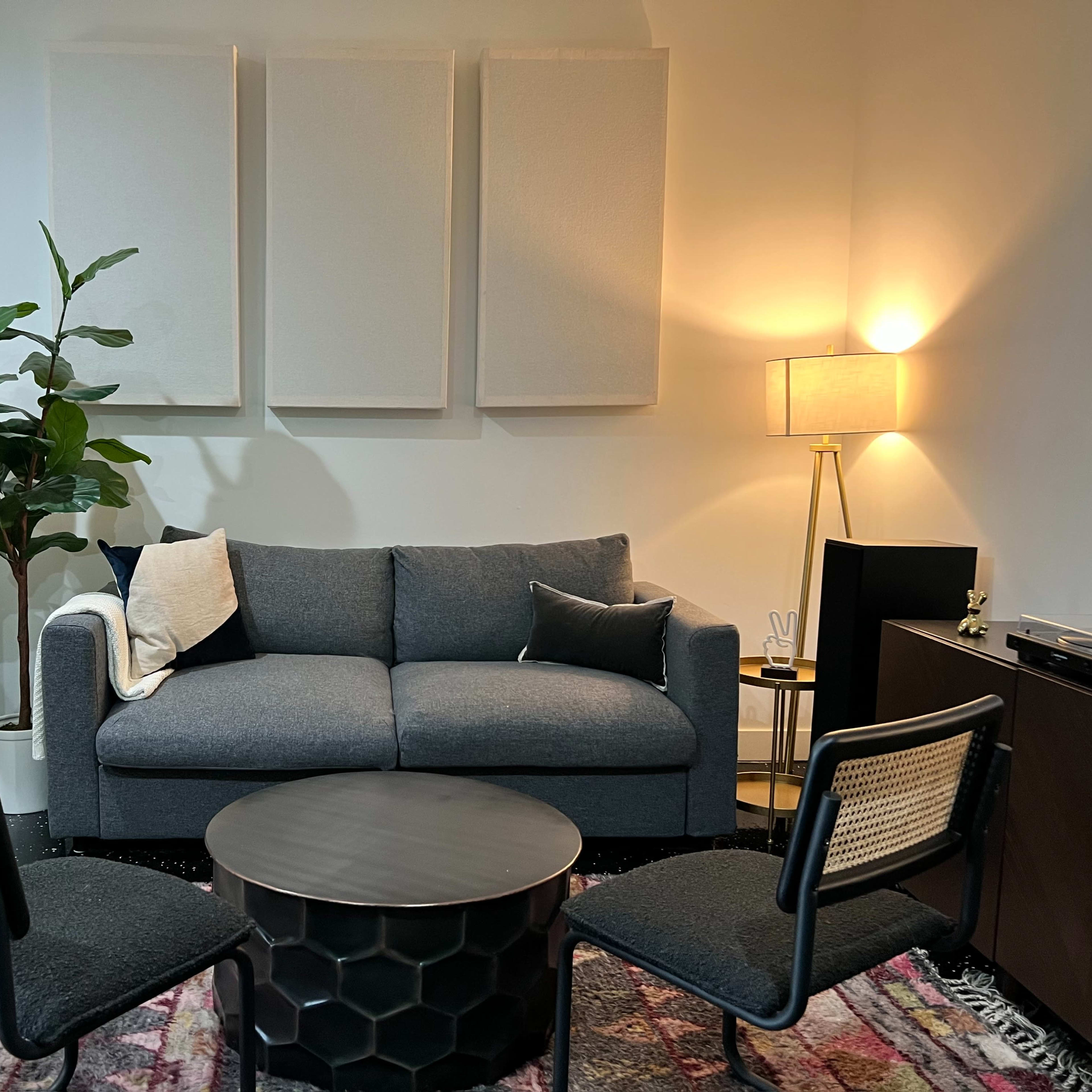 A modern living space featuring a gray sofa, two black accent chairs, a round coffee table, and a plant, with light-colored walls and a floor rug.