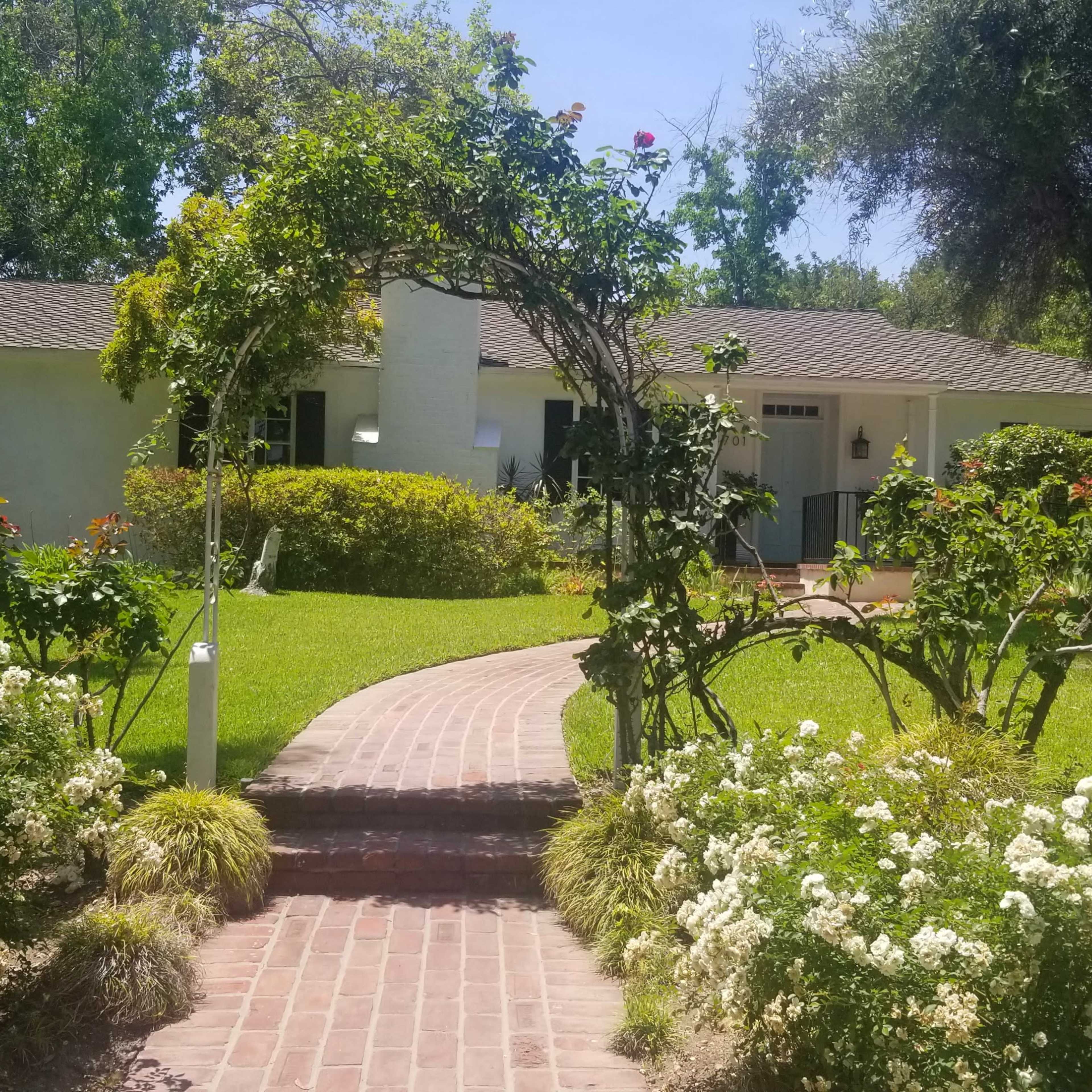 A brick pathway leads to a house surrounded by well-maintained gardens and greenery.