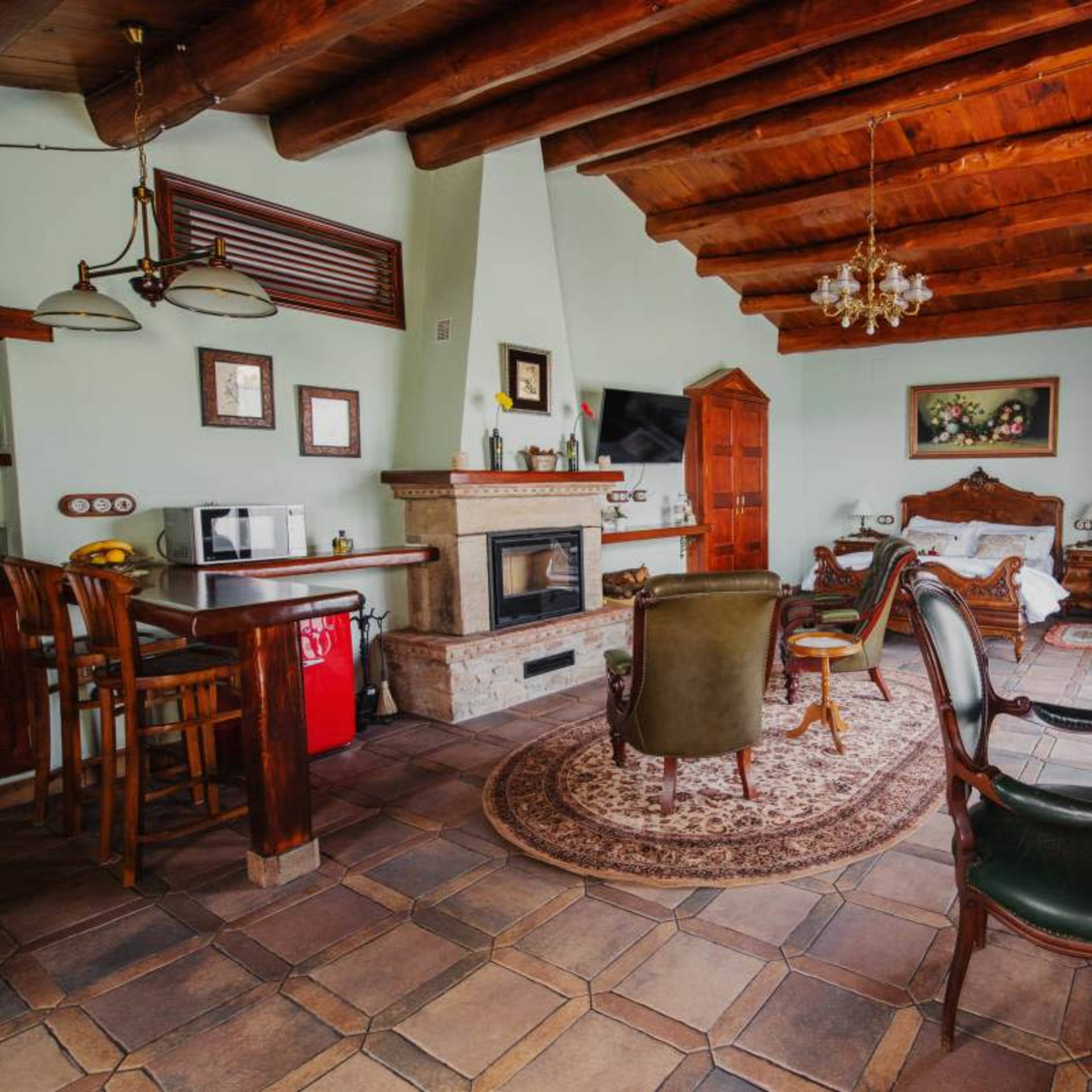 A cozy living room with wooden beams, a fireplace, and a mix of antique furniture including a bed, chairs, and a small dining table.