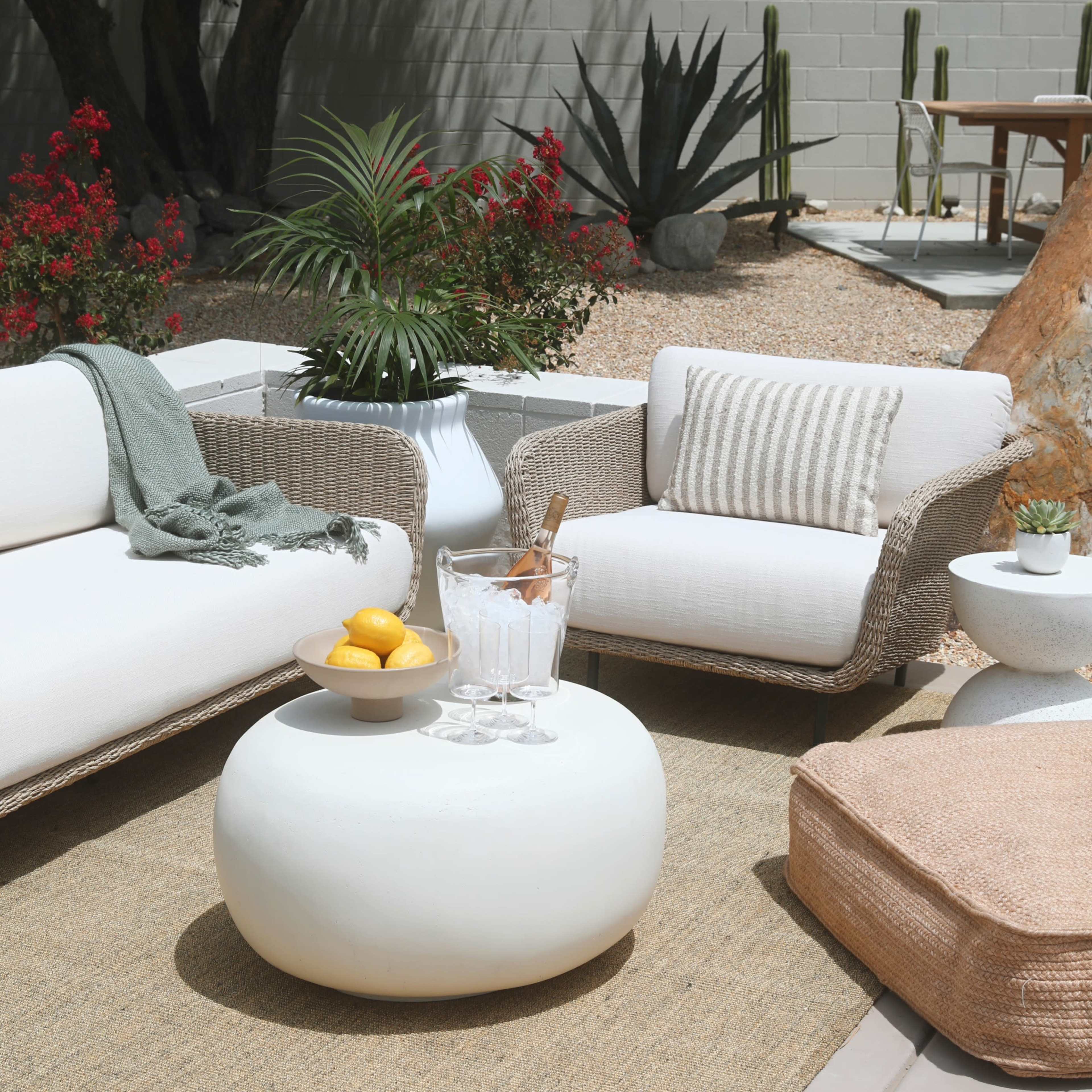 A cozy outdoor seating area features two couches, a round coffee table, and decorative elements like a plant and a bowl of lemons.