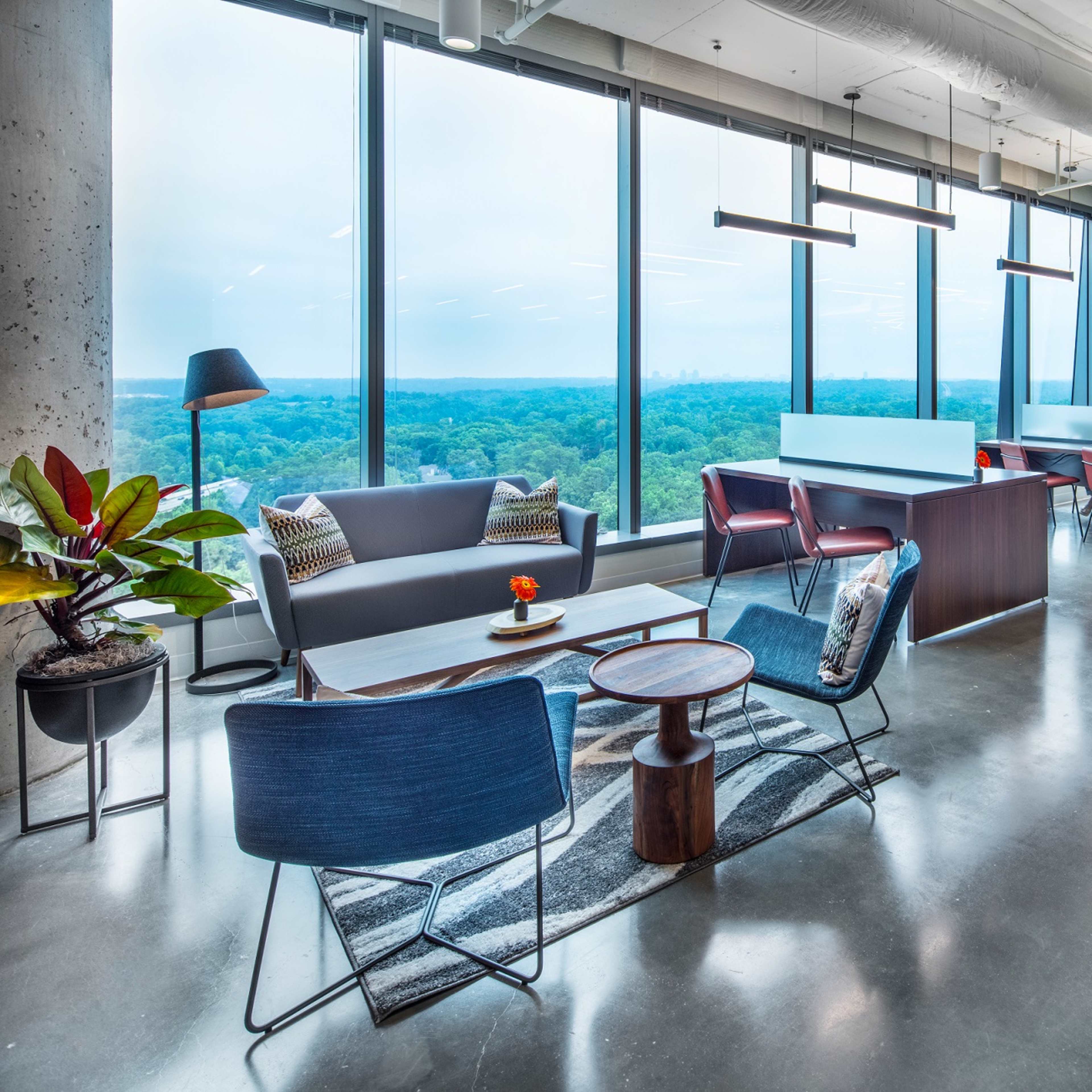 A modern office space with large windows offering a view of a city skyline, featuring various seating areas and plants.