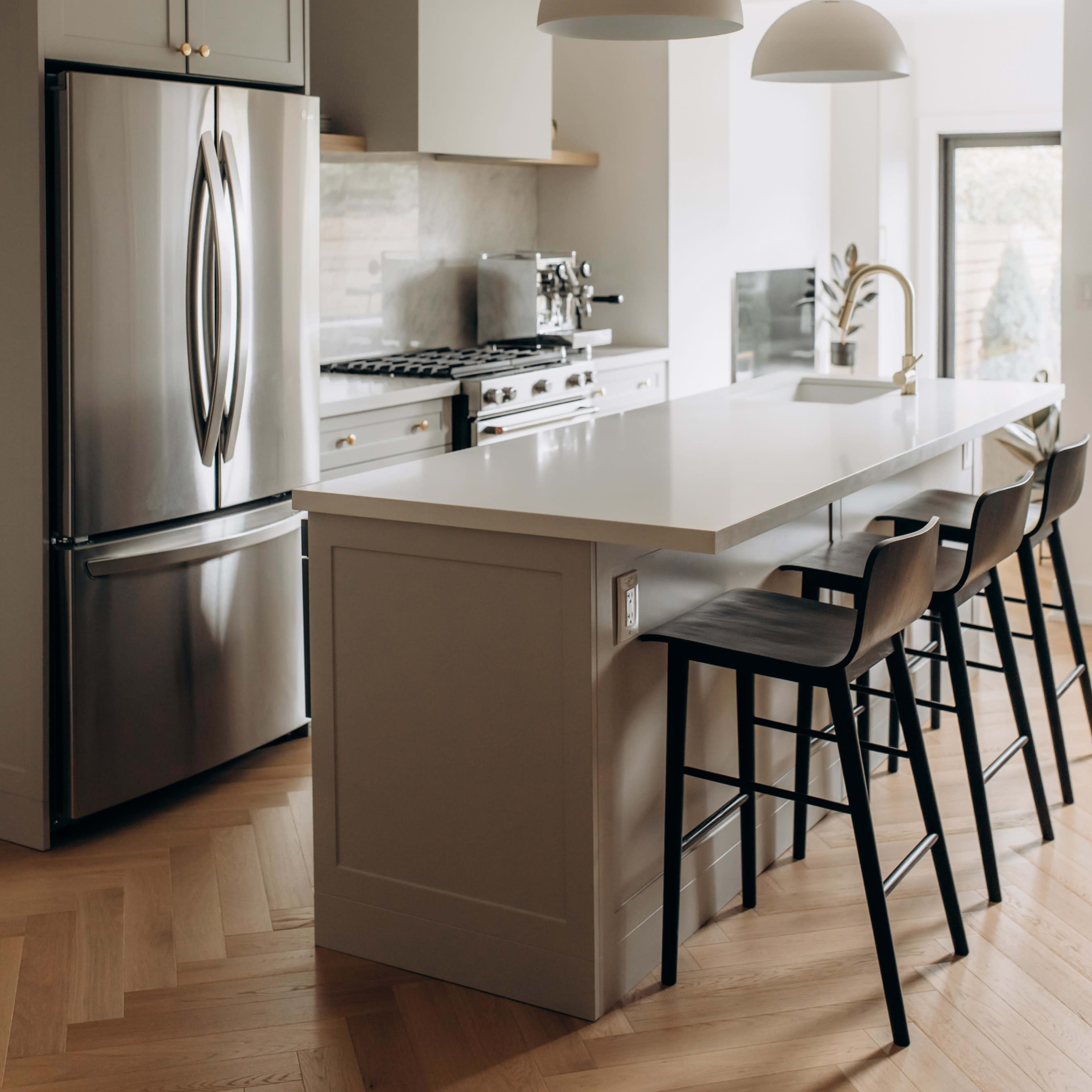 A modern kitchen featuring stainless steel appliances, a large island with seating, and pendant lights hanging above.