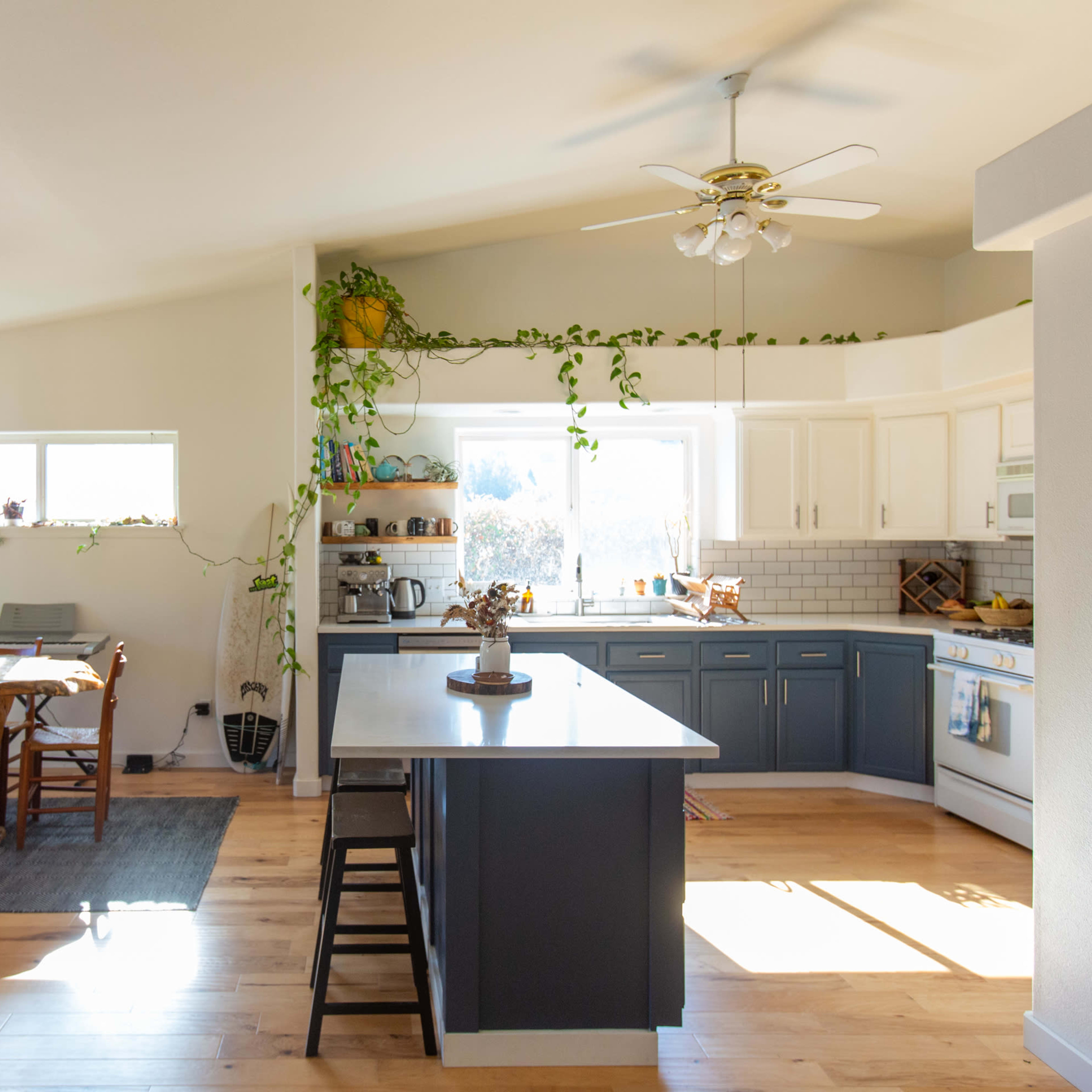 A bright kitchen features a central island, white cabinetry, and a dining area with wooden chairs and a table near a large window.
