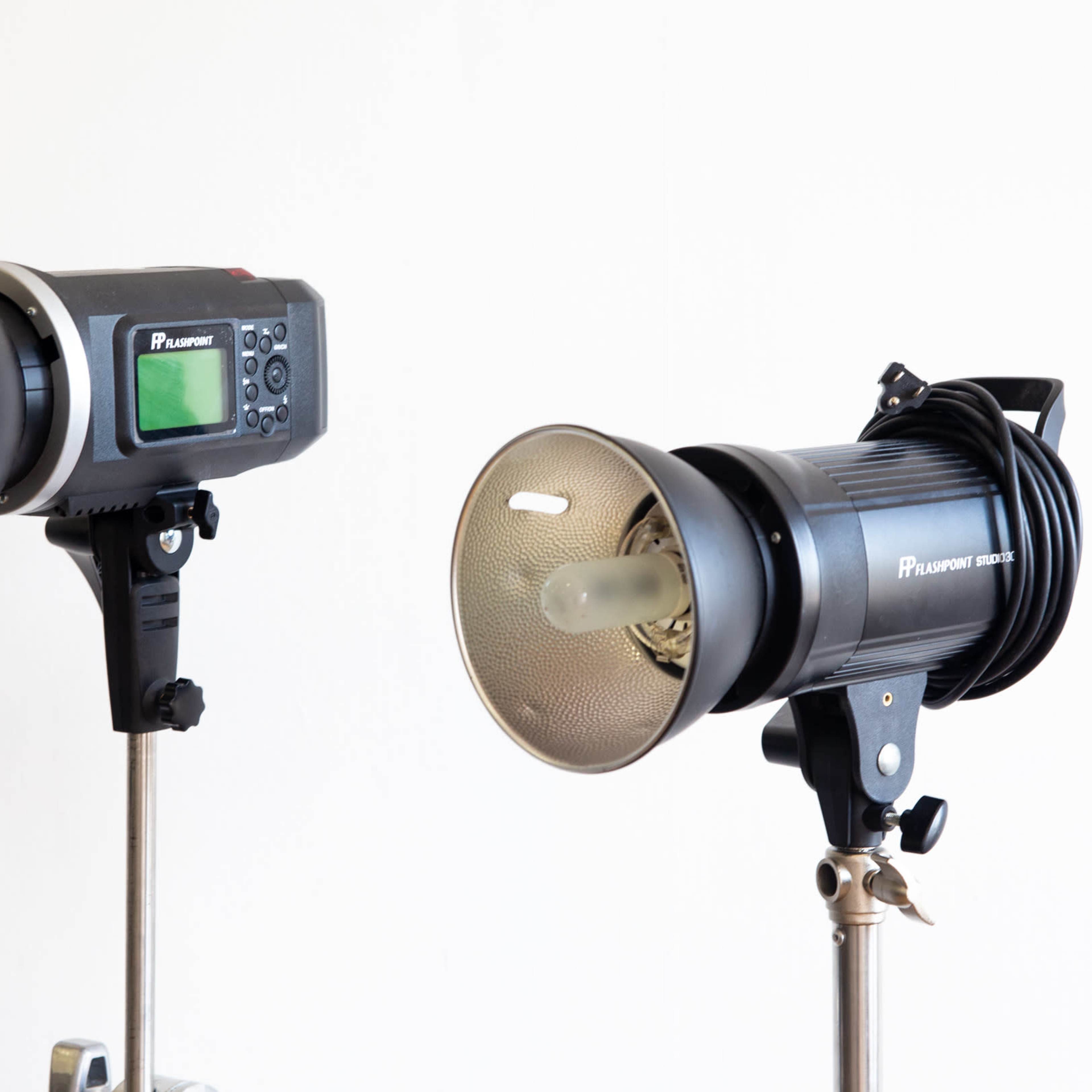 Two studio lighting equipment units mounted on tripods against a plain white background.