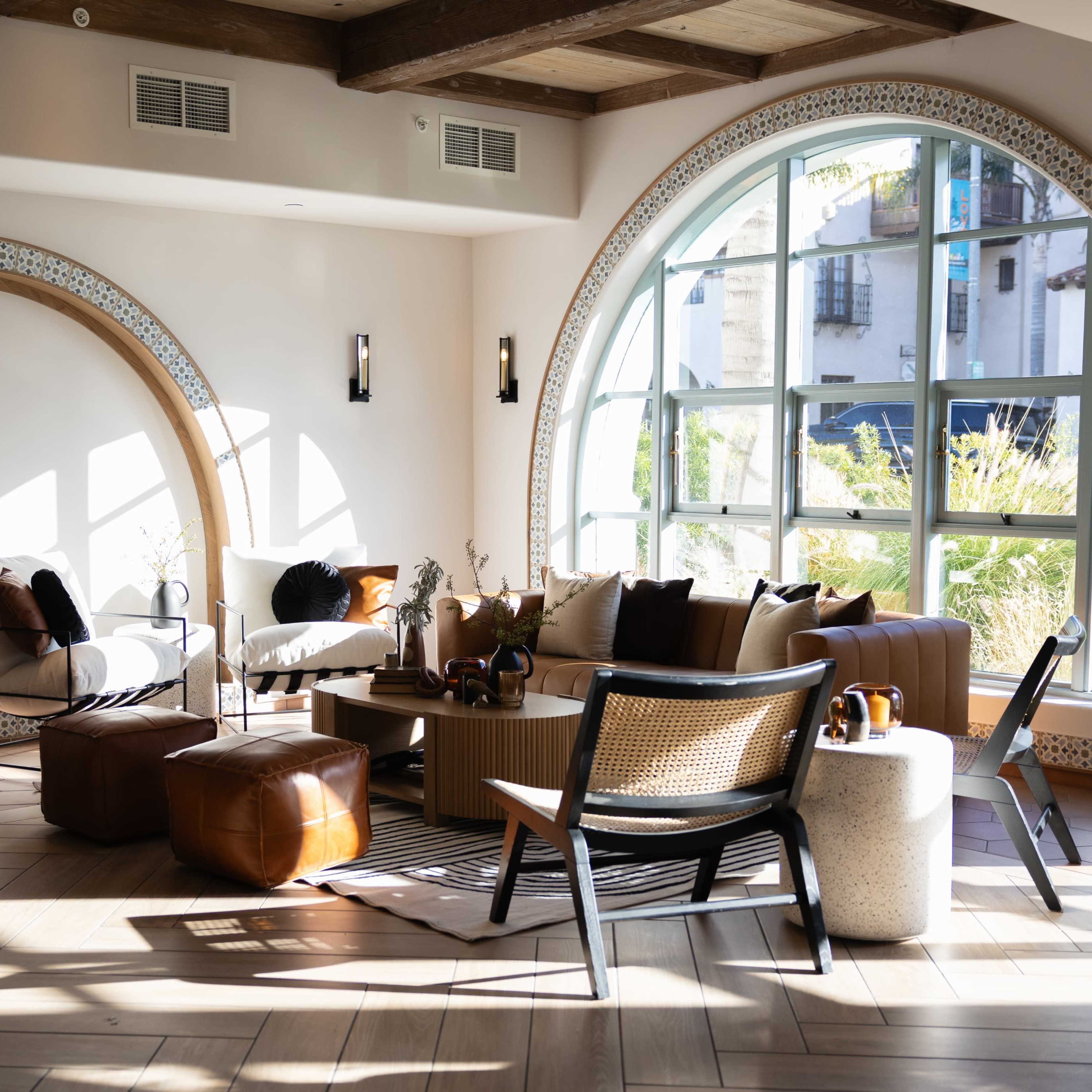 A well-lit modern lounge area featuring a mix of seating options, including armchairs and a sectional sofa, next to large arched windows.