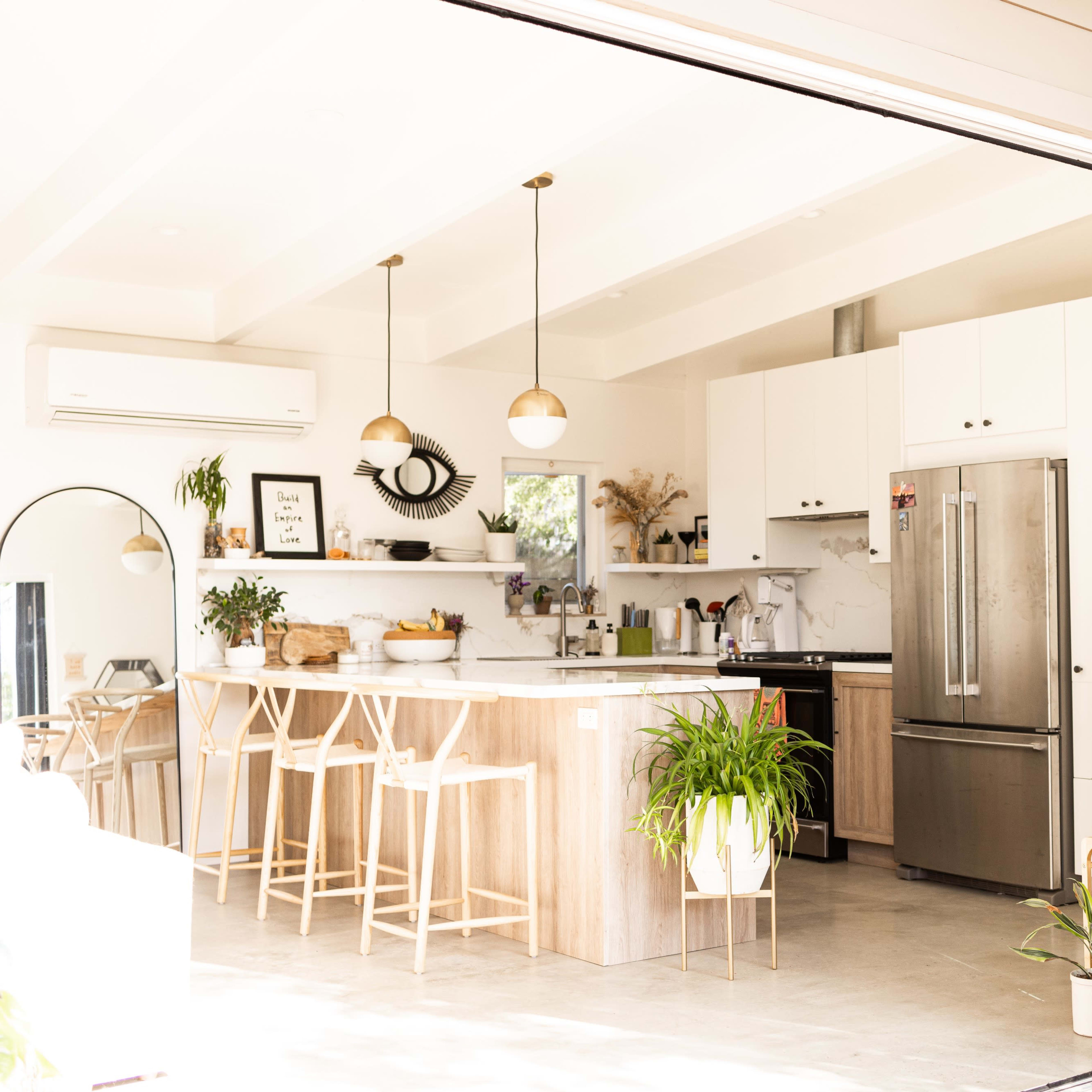 A modern kitchen with a large island, bar stools, and stainless steel appliances is visible through open glass doors.