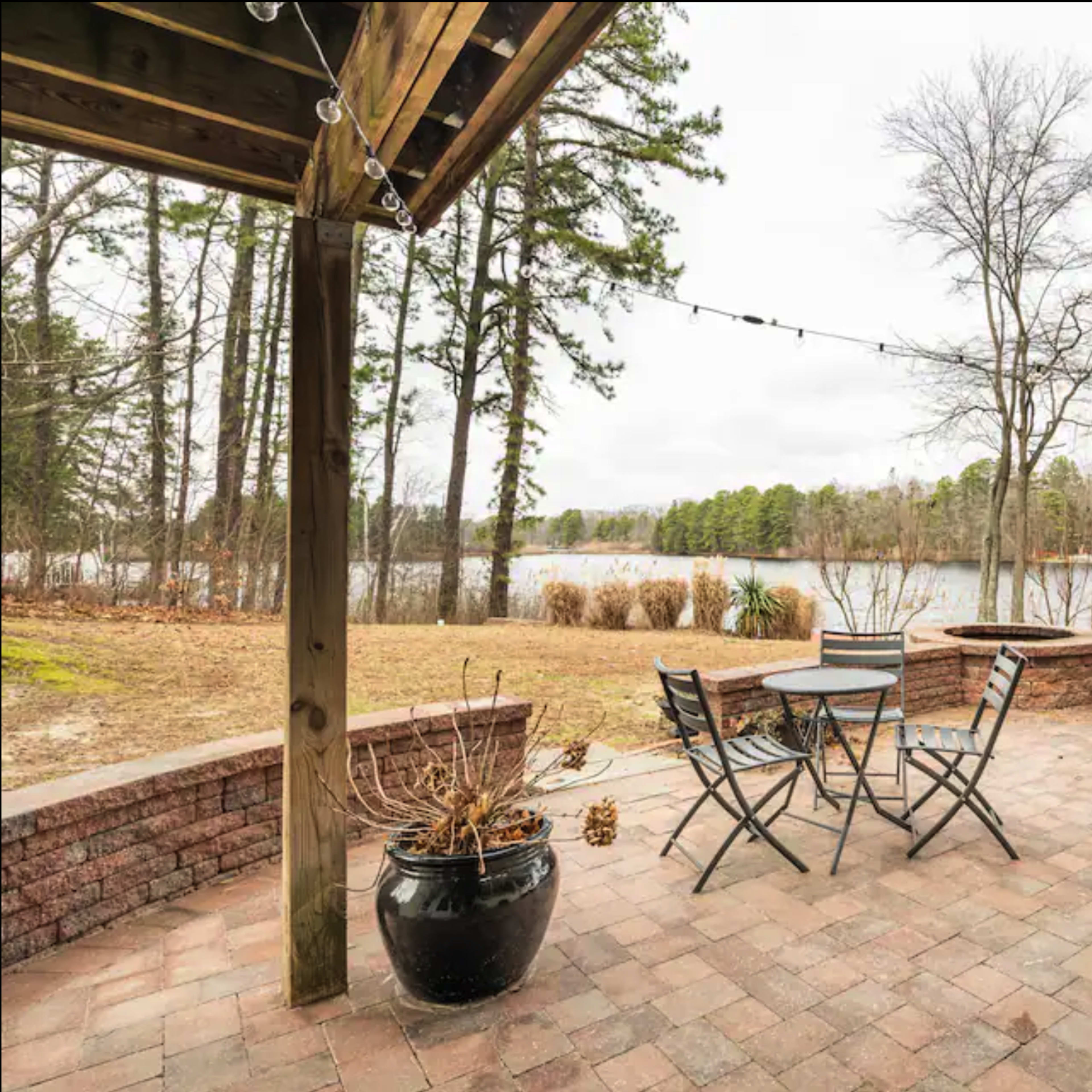 A patio with a table and chairs overlooks a calm lake surrounded by trees.