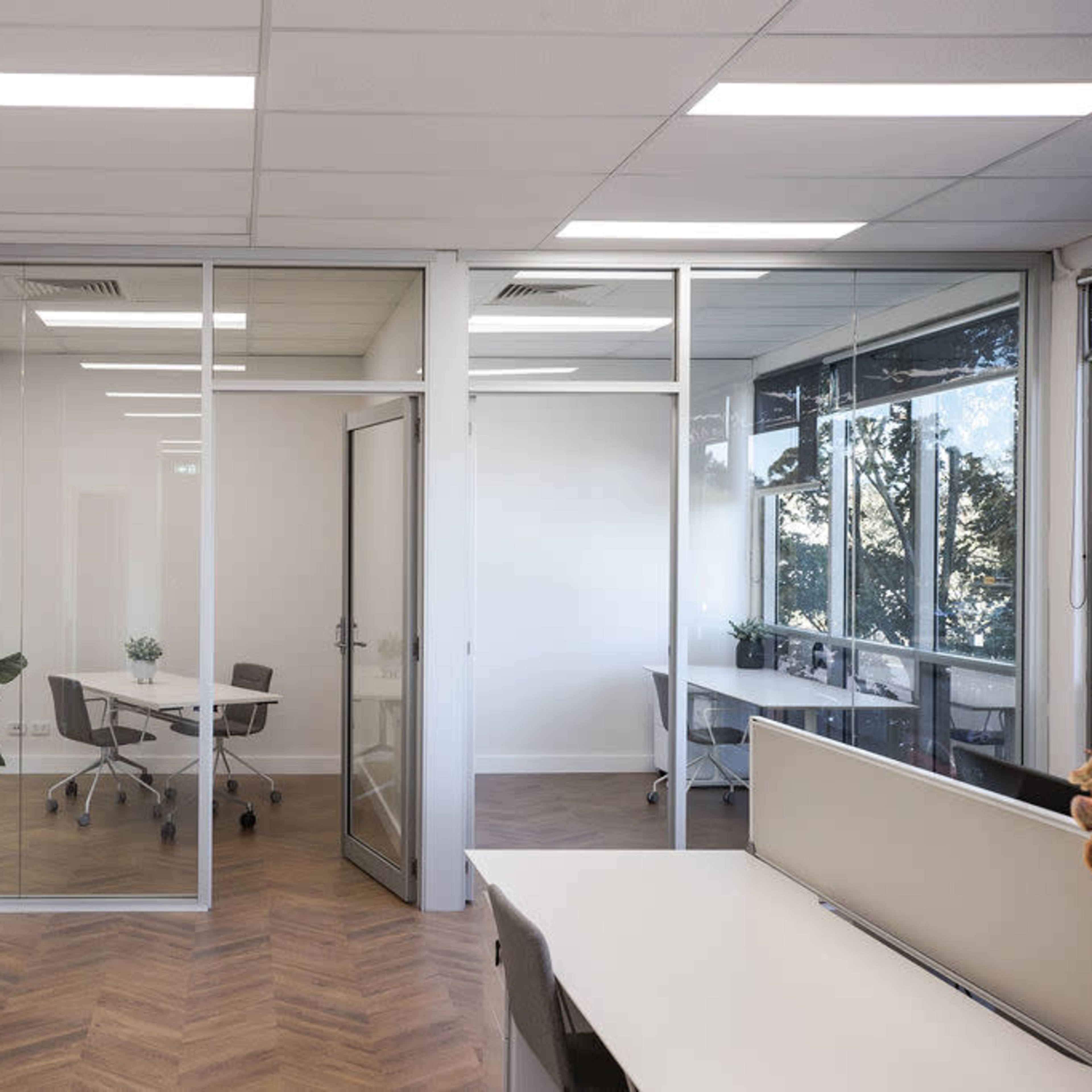 A modern office space with a glass-walled meeting room and desks arranged in a bright, open area.