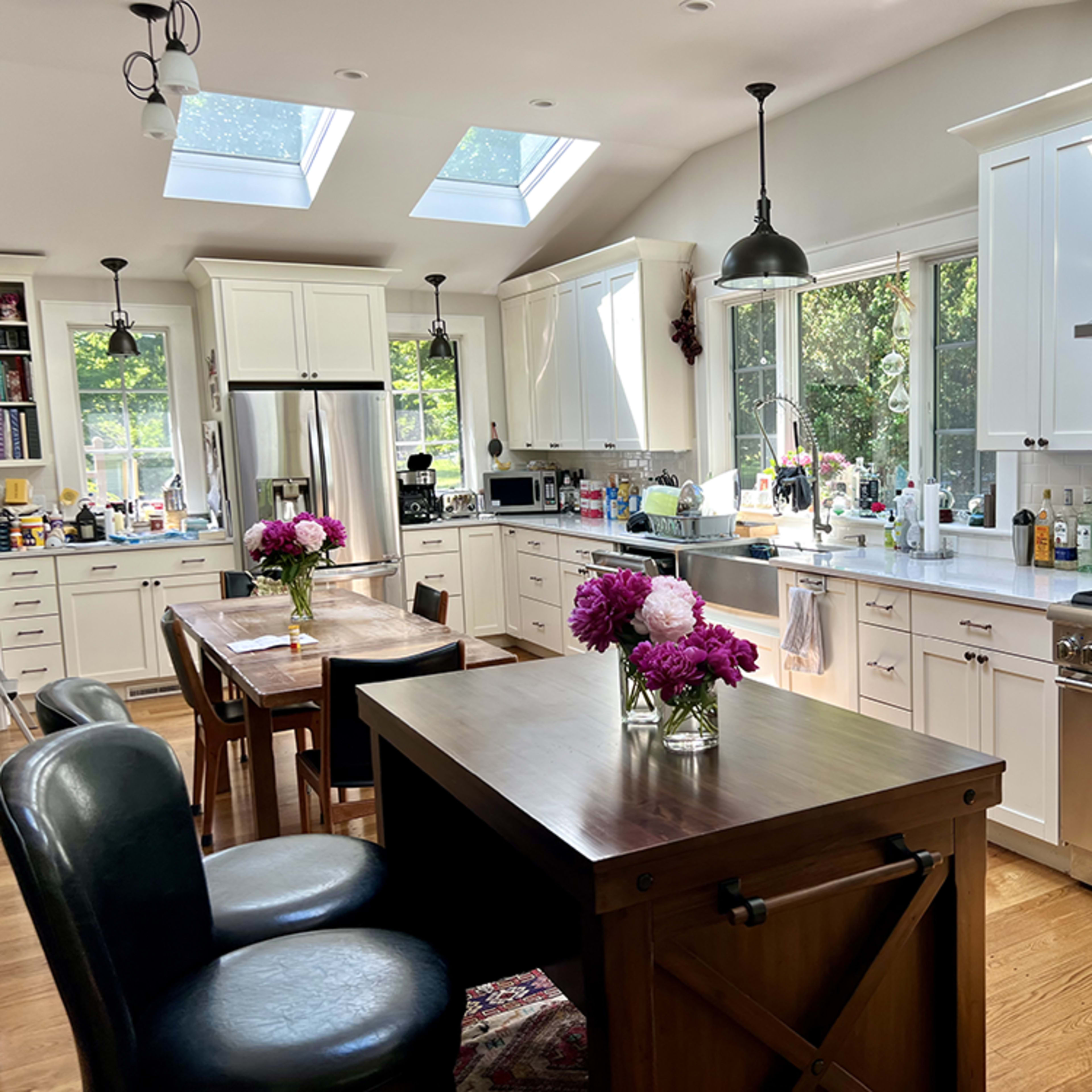 A spacious kitchen features white cabinetry, a large island with a wooden table, and skylights that illuminate the room.