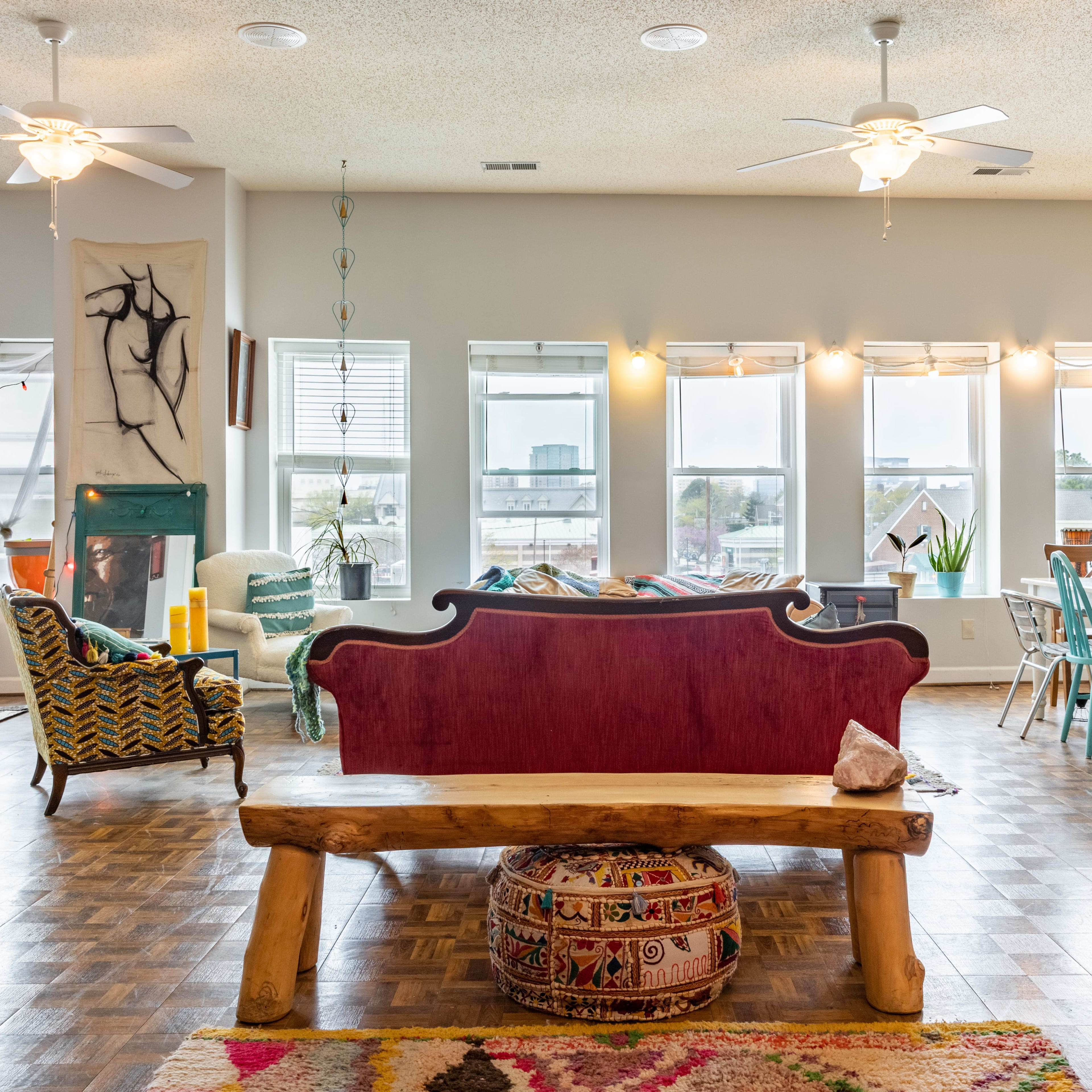 A spacious, brightly lit interior of a modern living area with a wooden bench, patterned textiles, and a dining area featuring colorful chairs.