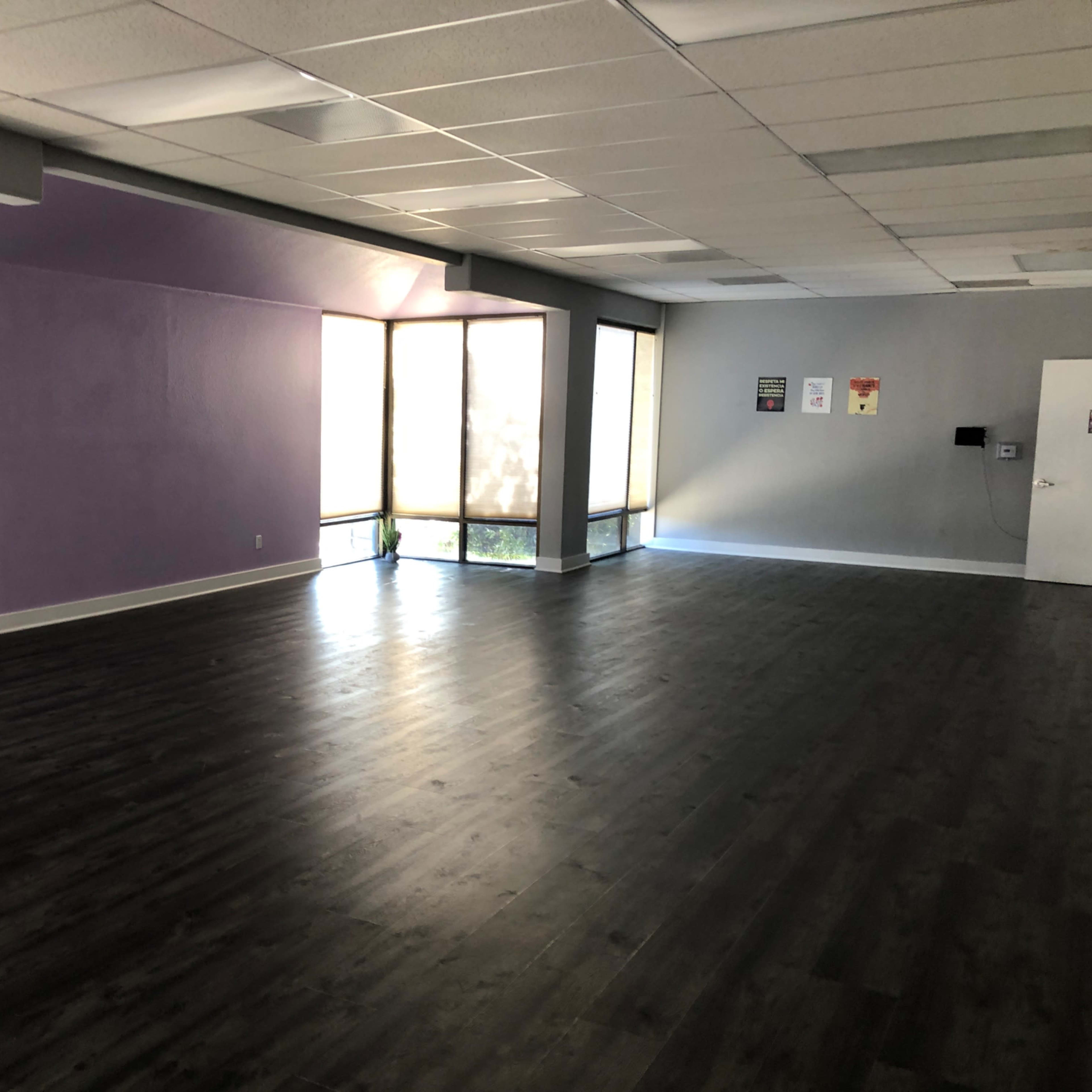 A vacant room with laminate flooring, purple walls, and large windows letting in natural light.