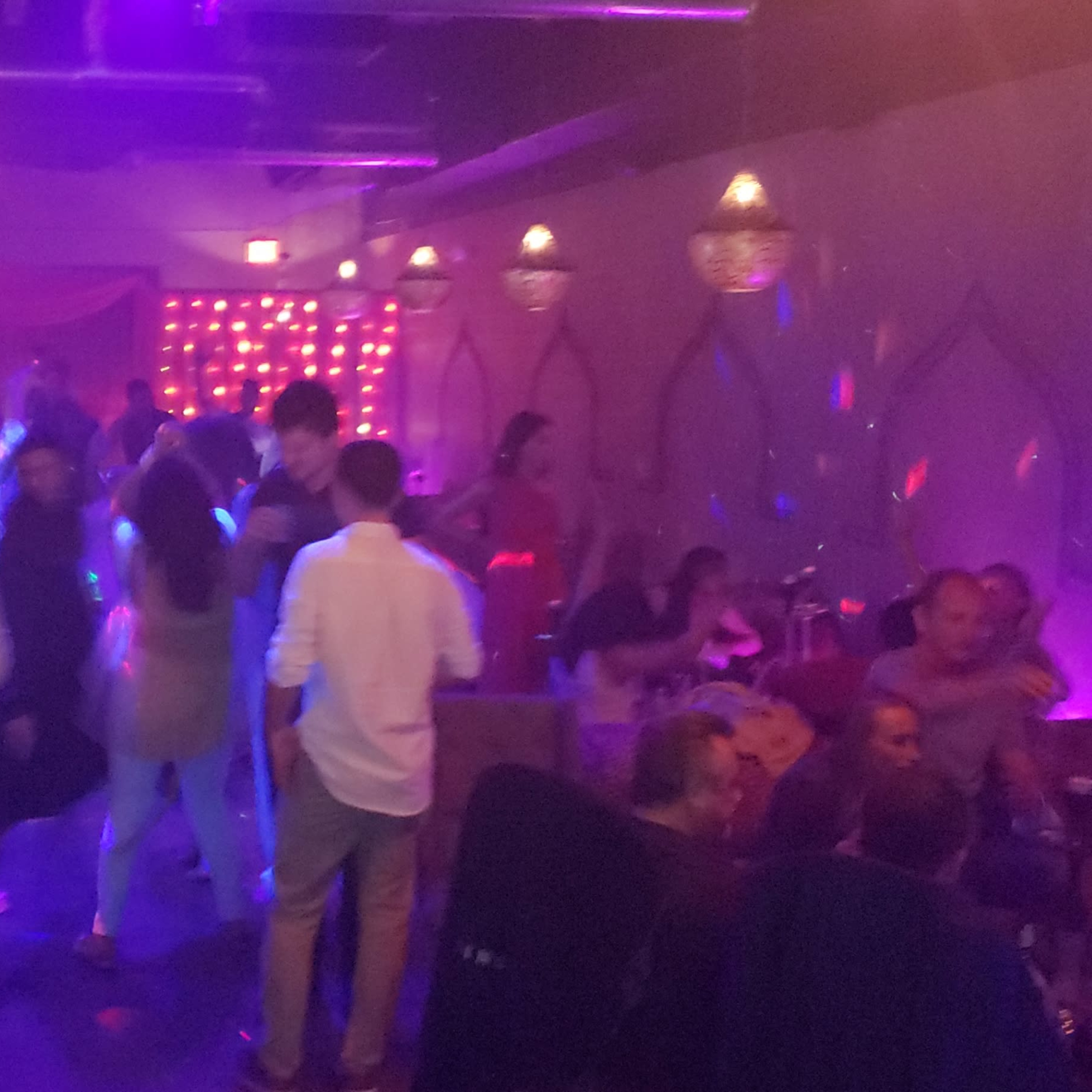 A lively nightclub scene features people dancing and socializing under colorful lights.