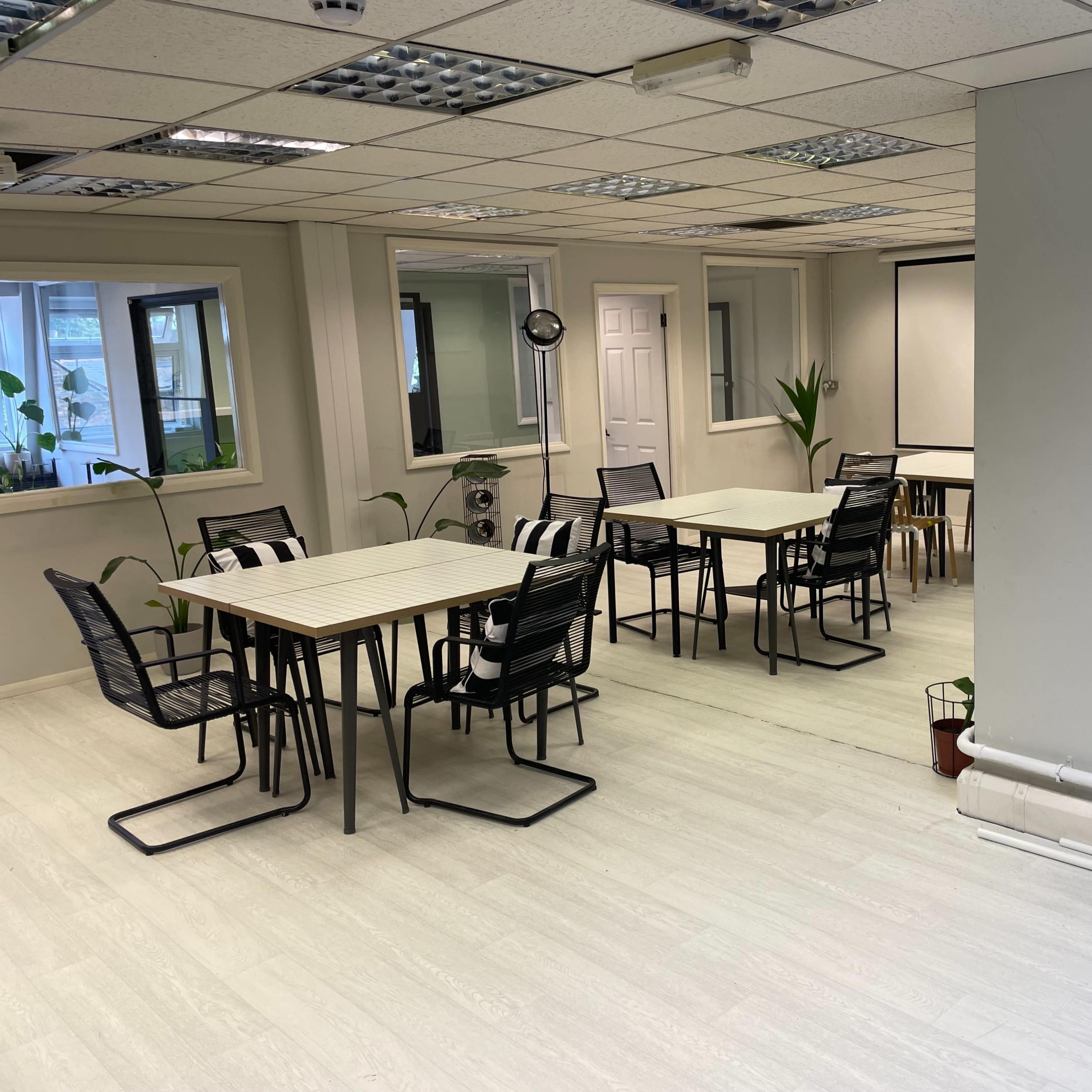 A brightly lit office space with several tables and chairs arranged neatly in a room with windows and plants.