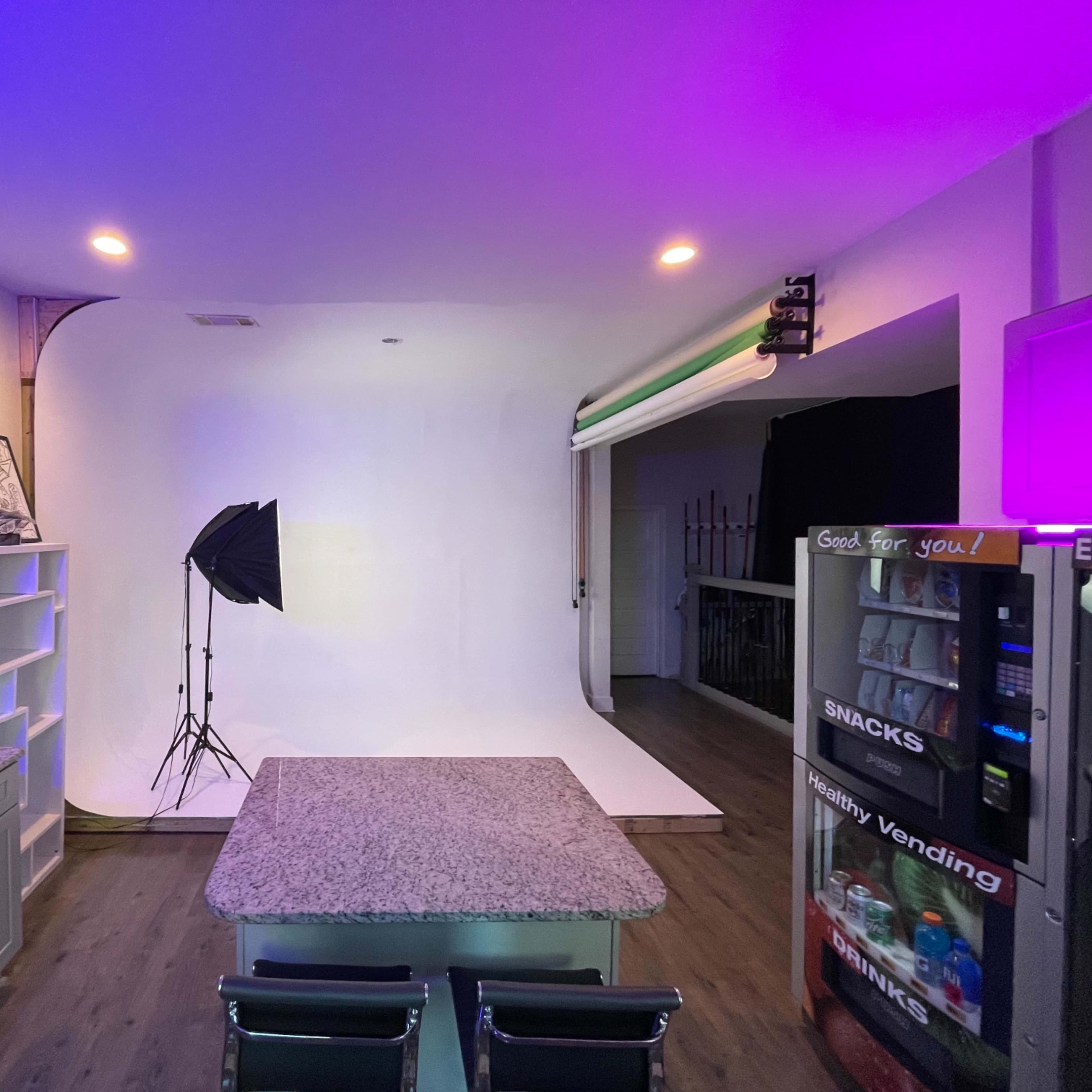 A modern kitchen with a large countertop, a photography backdrop and lighting setup, and a vending machine in the corner.