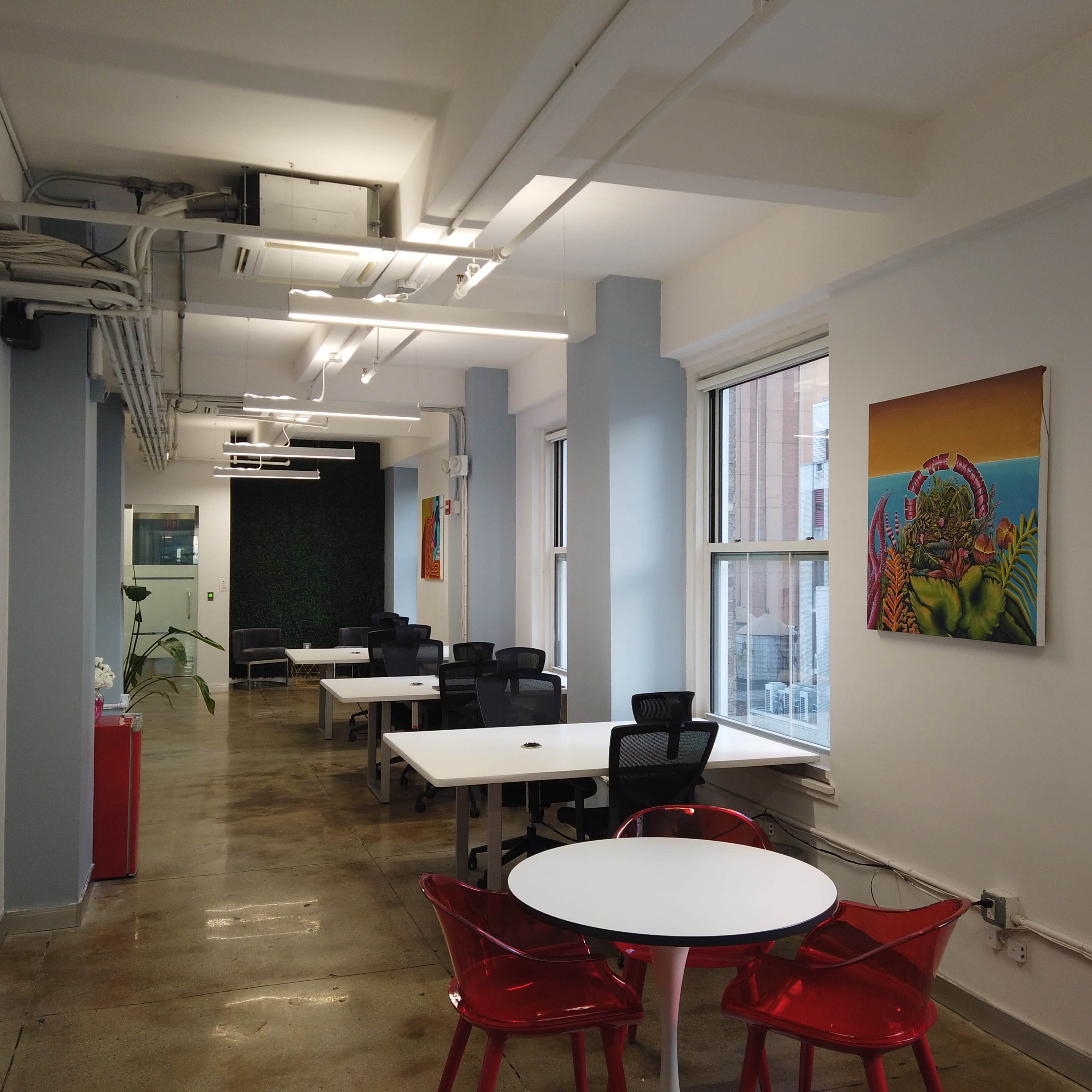A modern office space with white tables, black chairs, and colorful wall art, illuminated by overhead lighting.