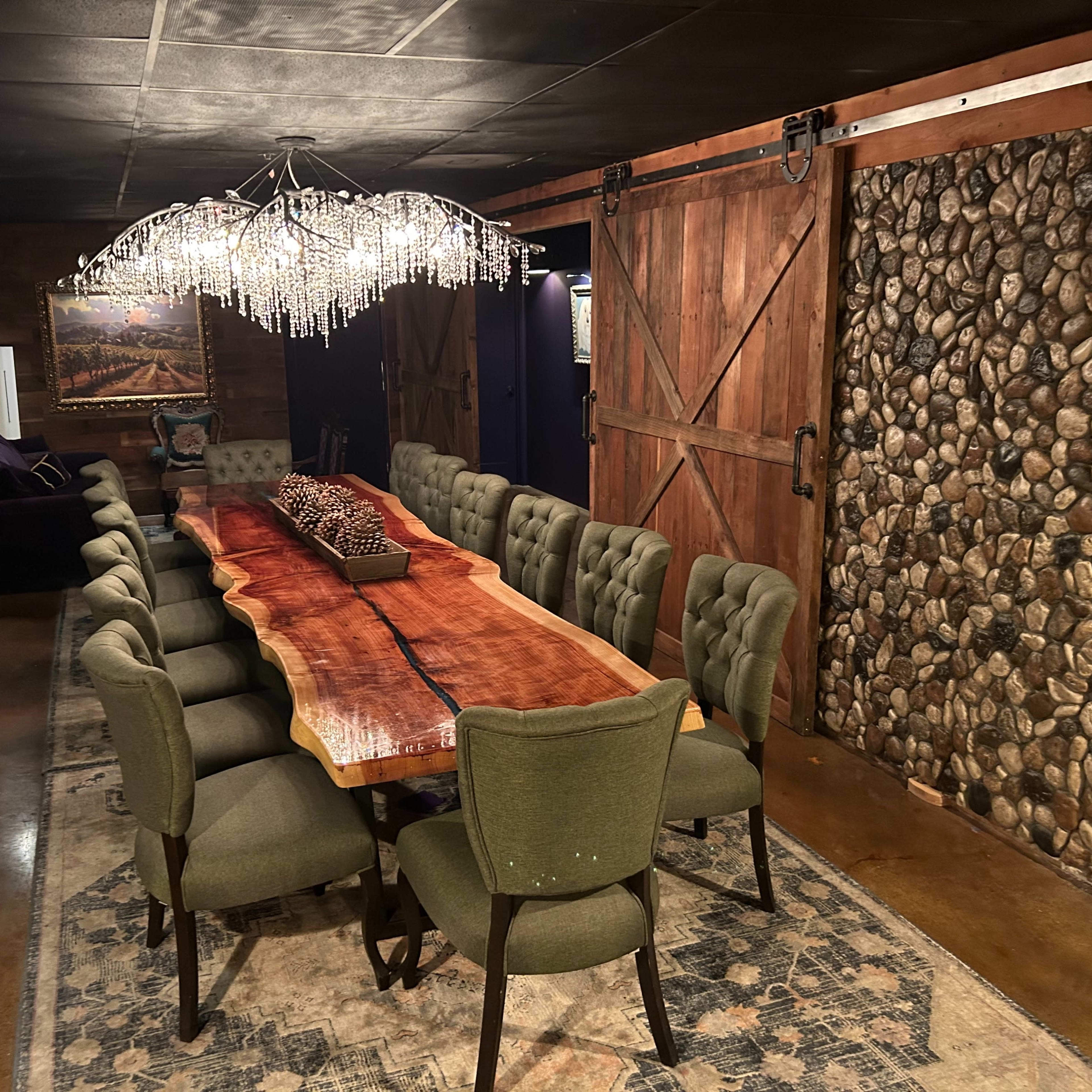 A large wooden dining table surrounded by ten green upholstered chairs in a room with rustic wooden walls and a chandelier made of crystals.