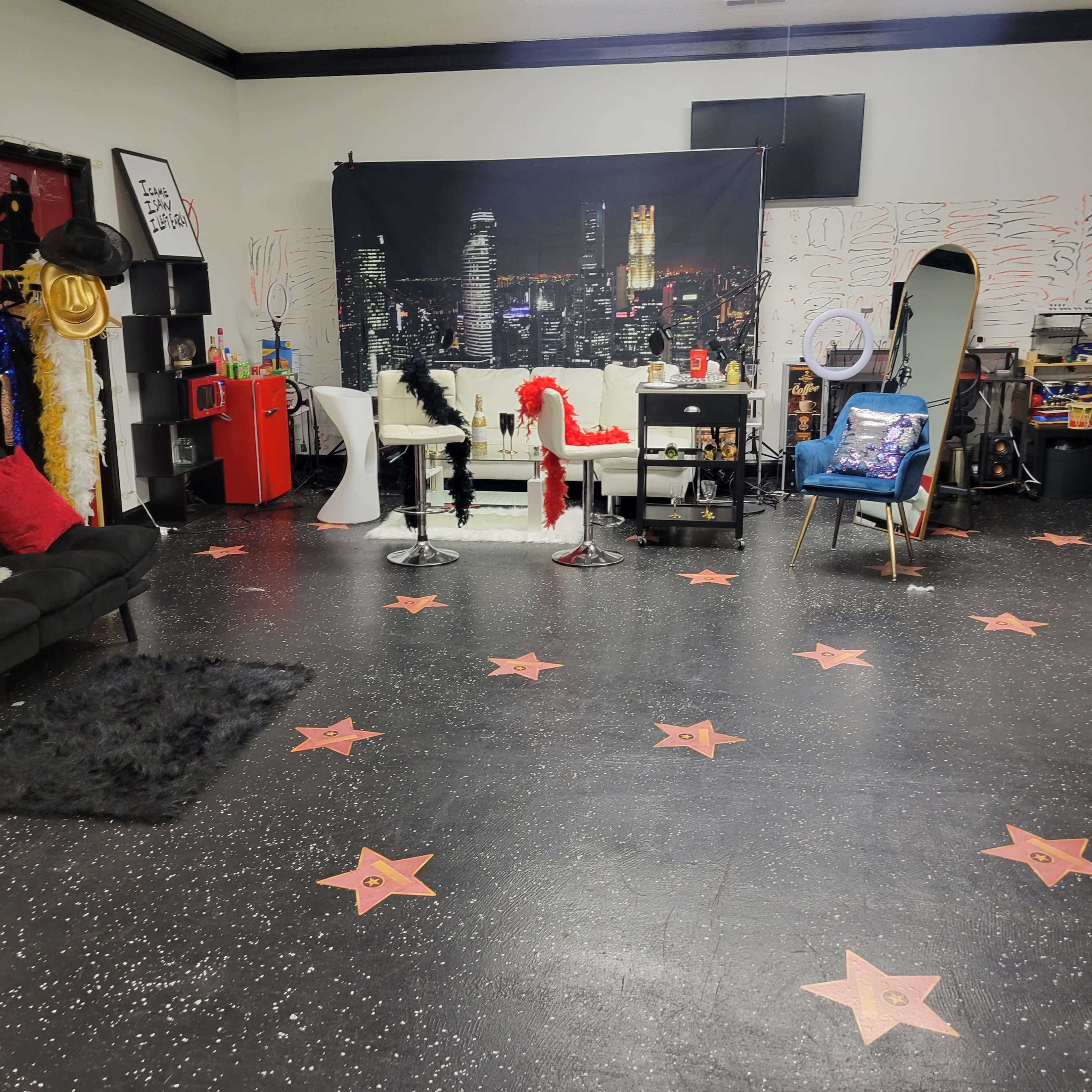 A spacious, decorated room with a black floor featuring star patterns, various seating options, and a backdrop of a city skyline.