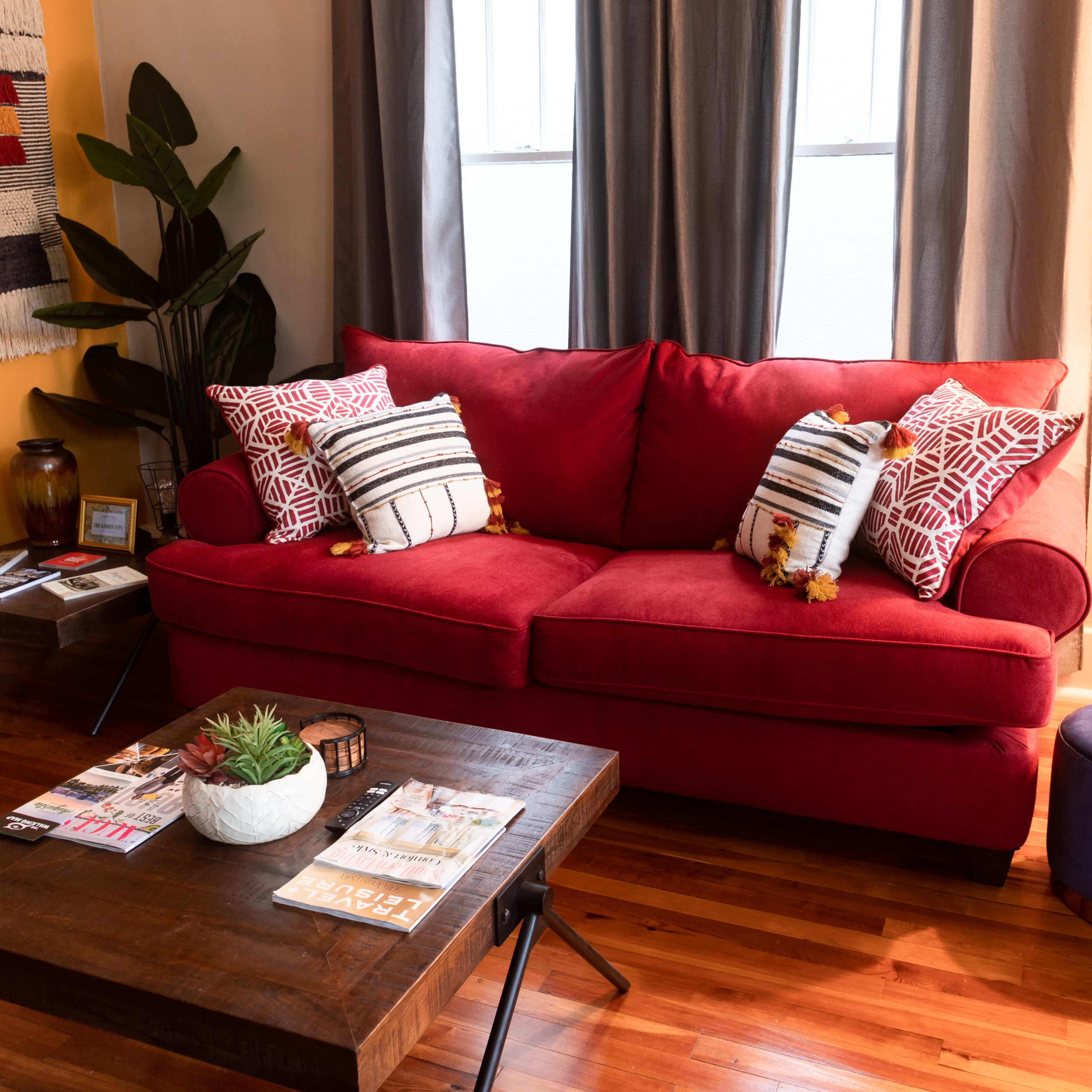 A red sofa is positioned next to a wooden coffee table, with decorative pillows, a plant, and a lamp illuminating the space.