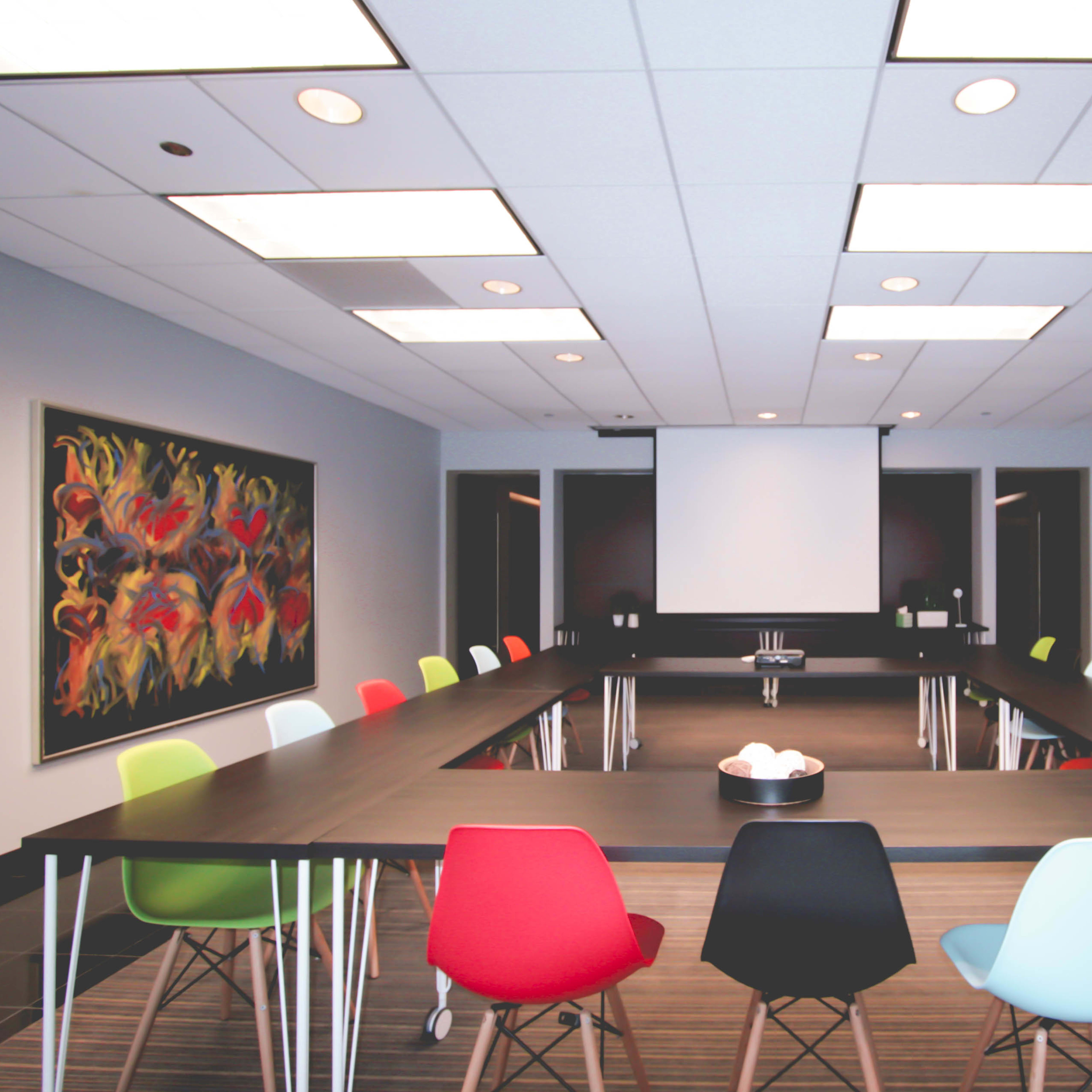 A large conference room features a long rectangular table surrounded by colorful chairs and a projection screen at one end.