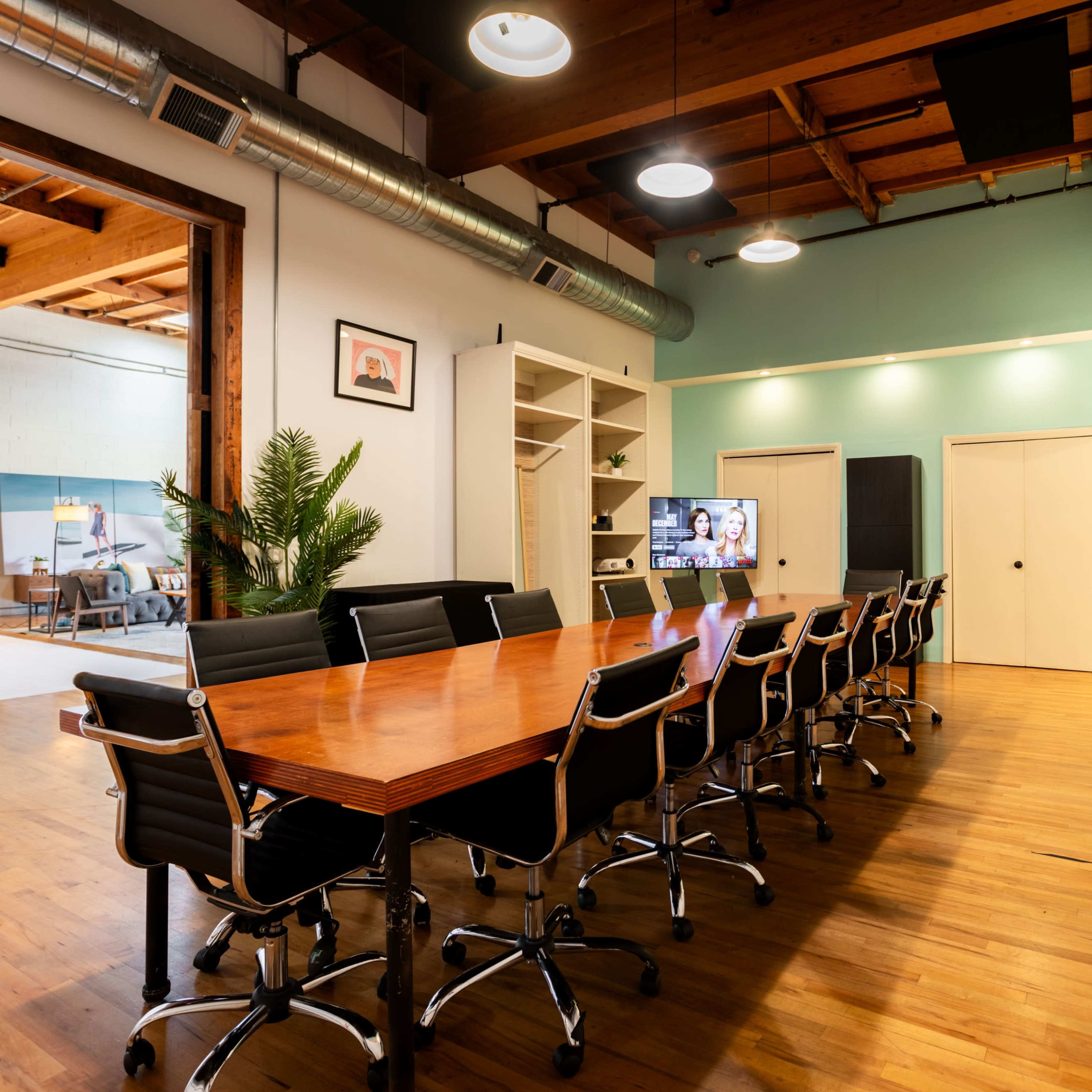 A large conference room features a long wooden table surrounded by black chairs, with a green wall and modern decor in the background.
