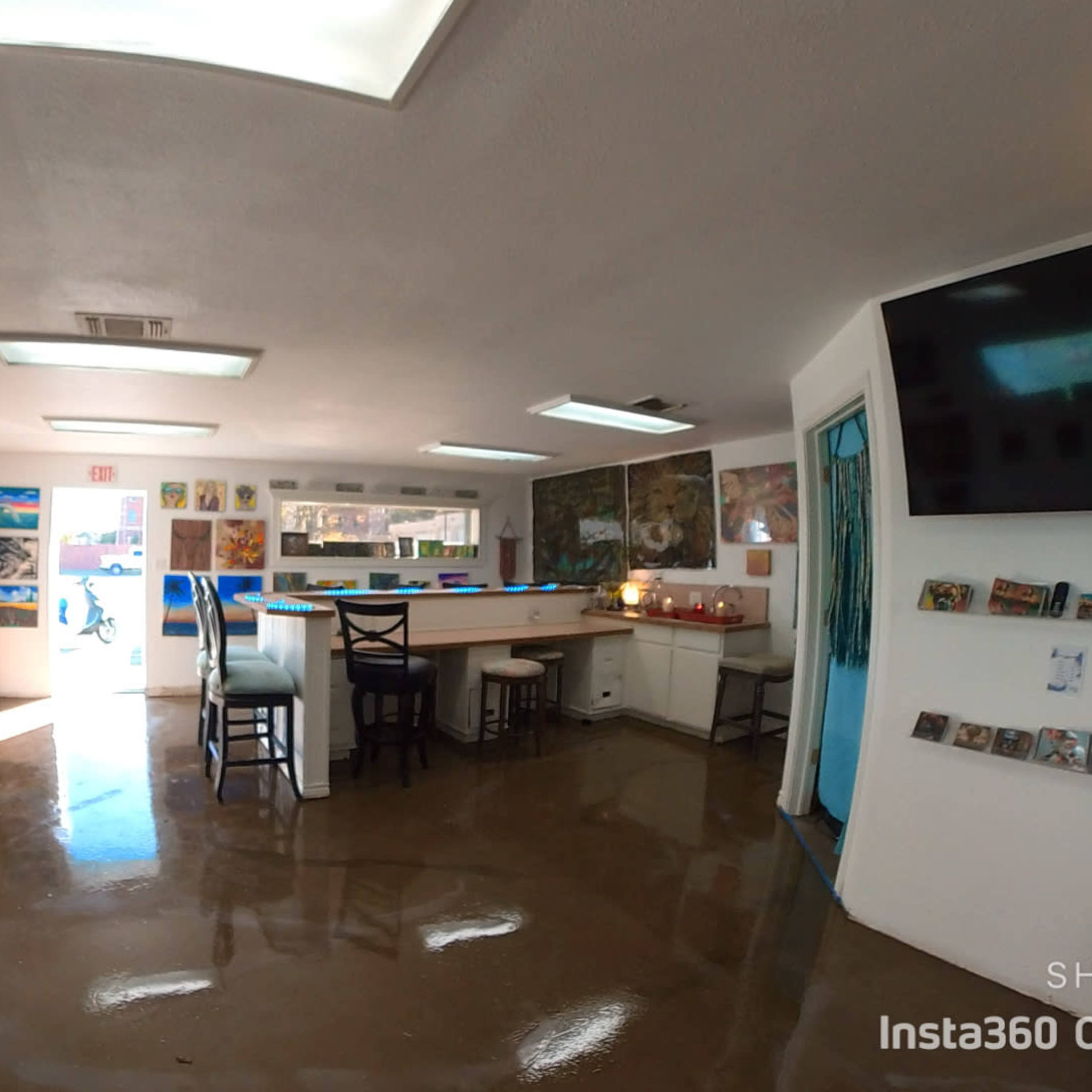 An art gallery interior with painted walls, a central seating area, and numerous artworks displayed on the walls.
