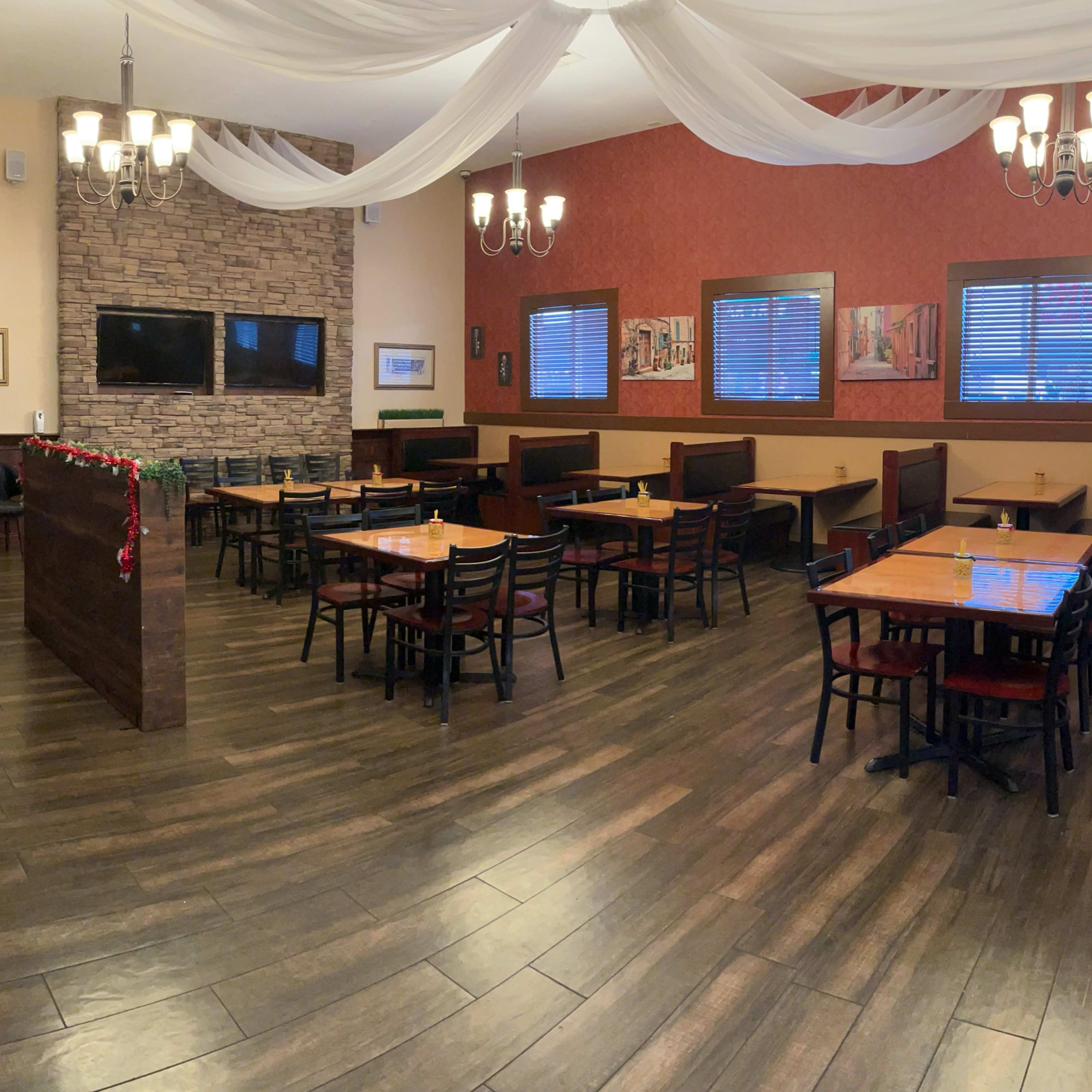 A restaurant interior with wooden tables and chairs arranged around a partially separated dining area, featuring stone and fabric decor.