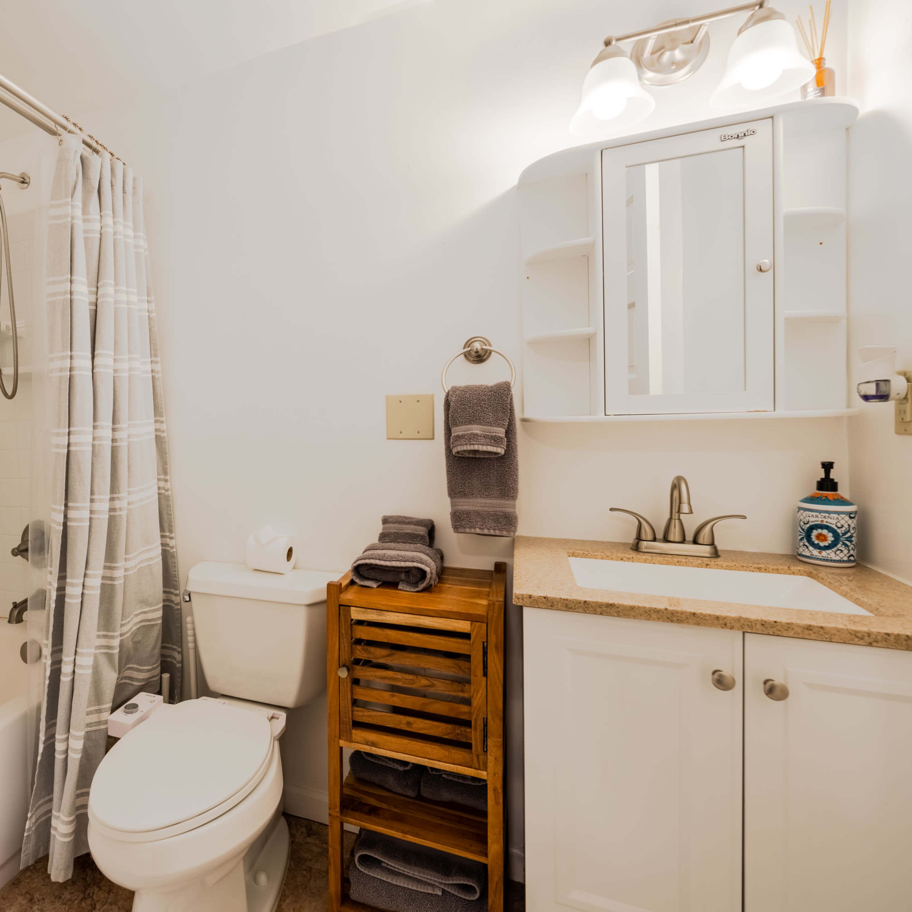 A bathroom featuring a bathtub with a shower, a toilet, a sink with a vanity mirror, and wooden shelving for towels.