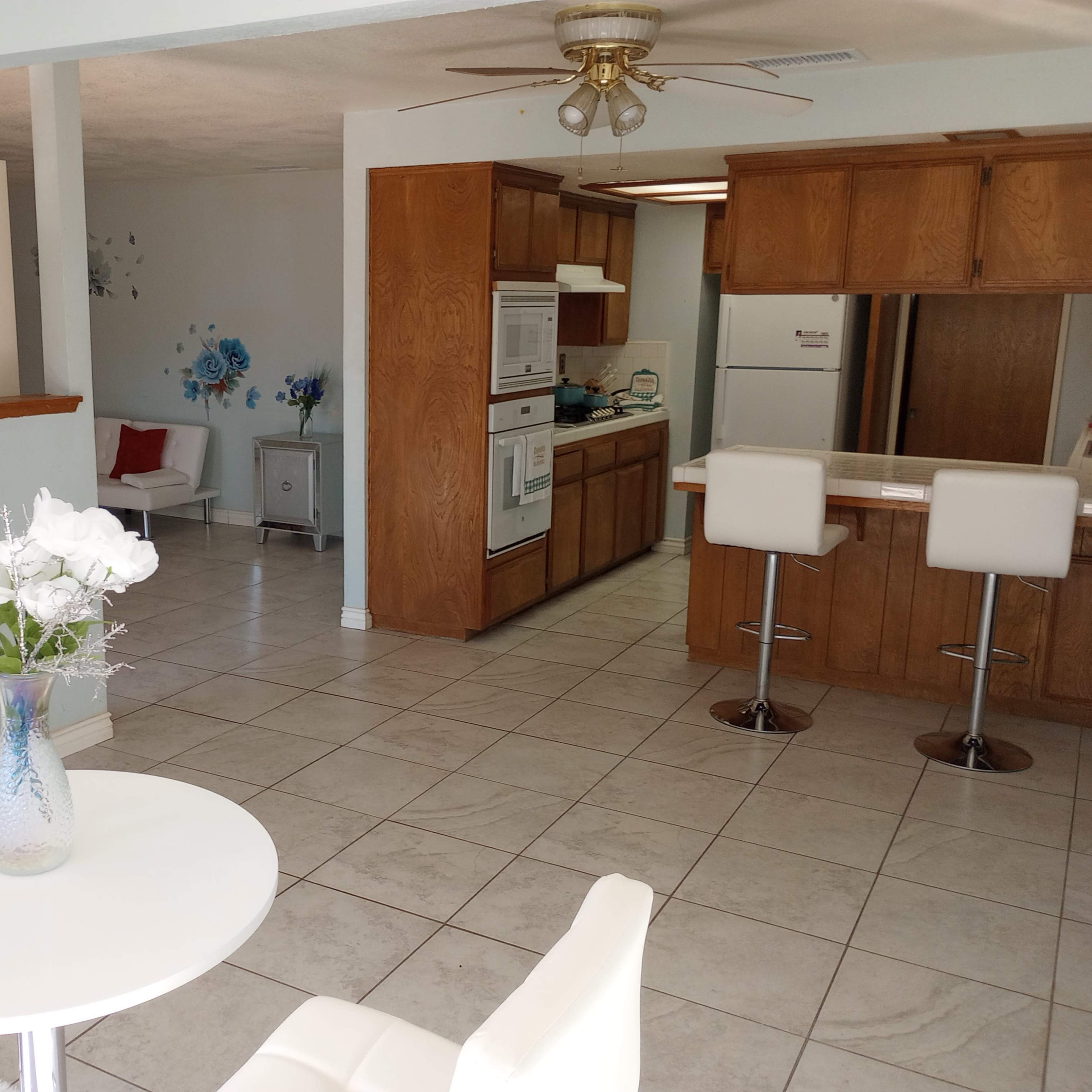 A small dining area with a white table and chairs is adjacent to a wooden kitchen with appliances and cabinetry.