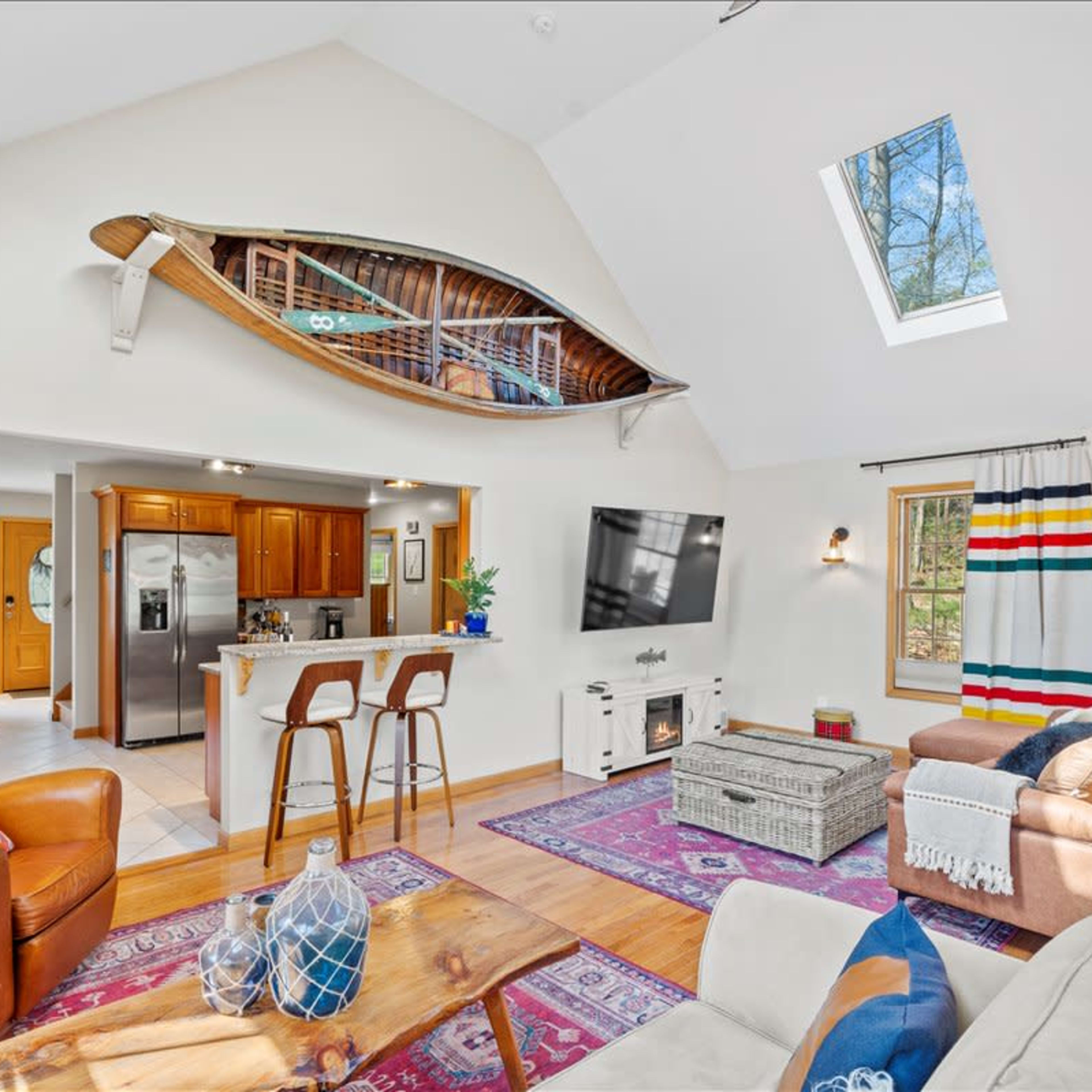 The living space features a high ceiling, a wooden canoe mounted on the wall, a cozy seating area, and a kitchen with modern appliances.