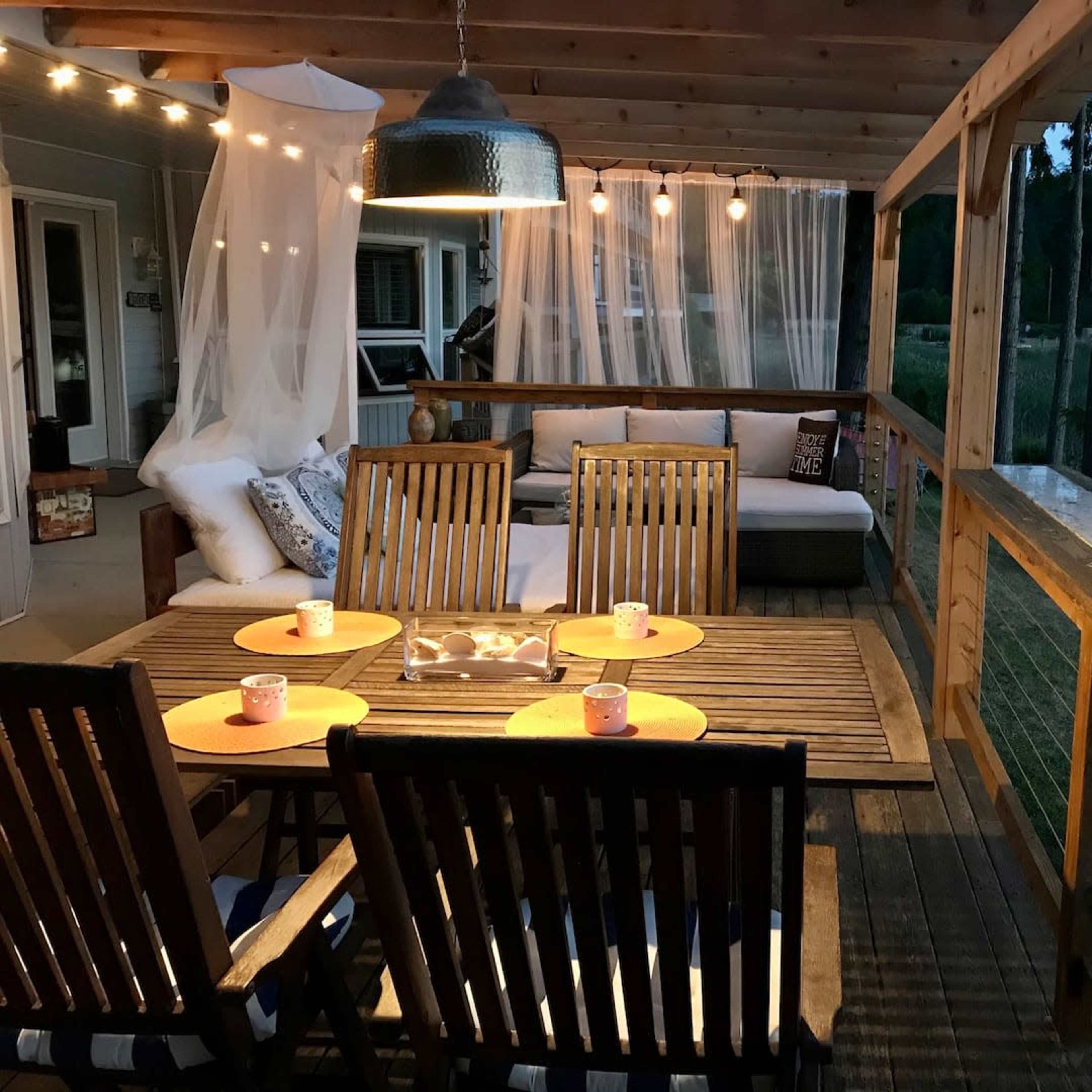 A wooden deck area with a table set for dining, surrounded by string lights and a cozy seating arrangement.