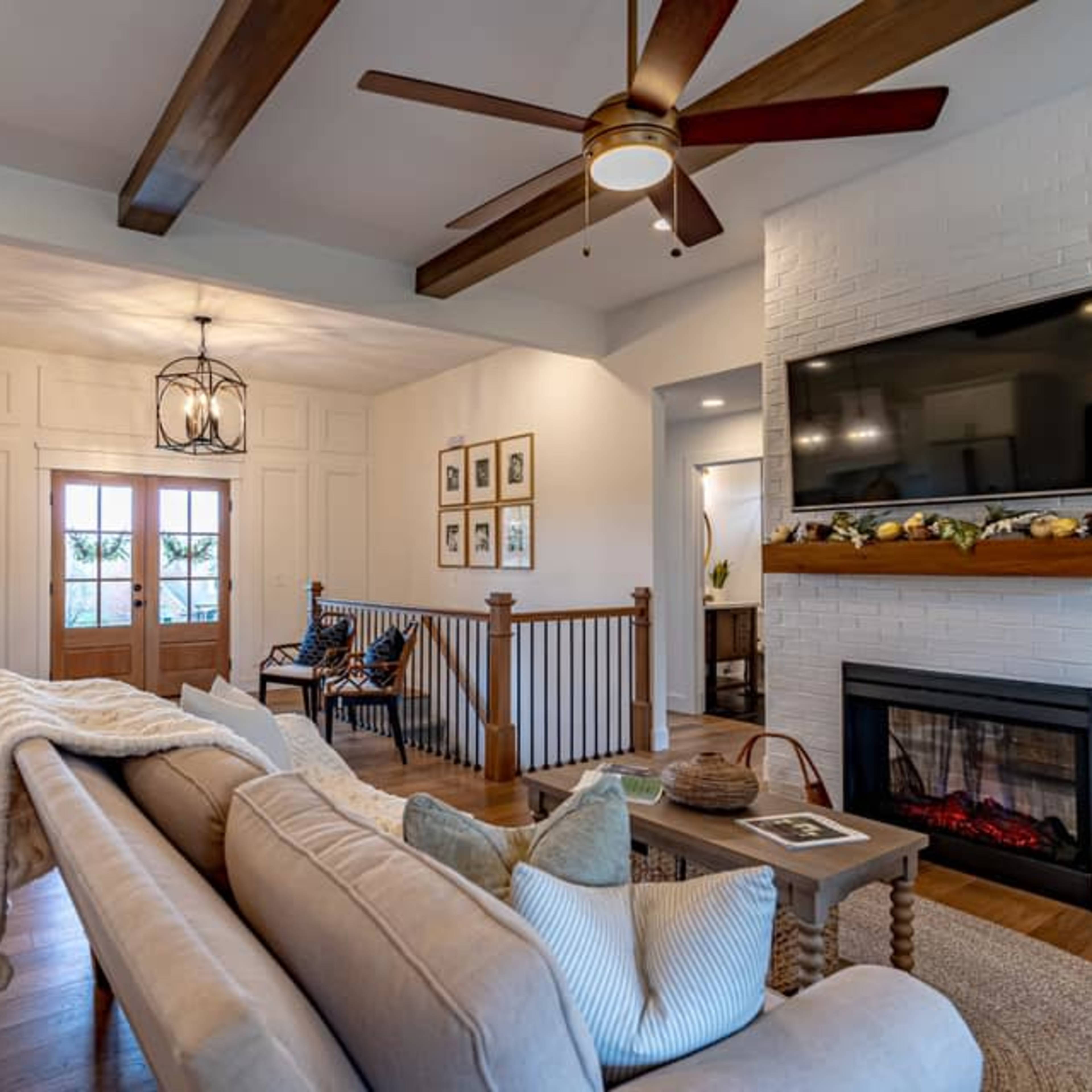 A living room with a sofa, fireplace, and wooden beams on the ceiling, featuring a front entrance with double doors.