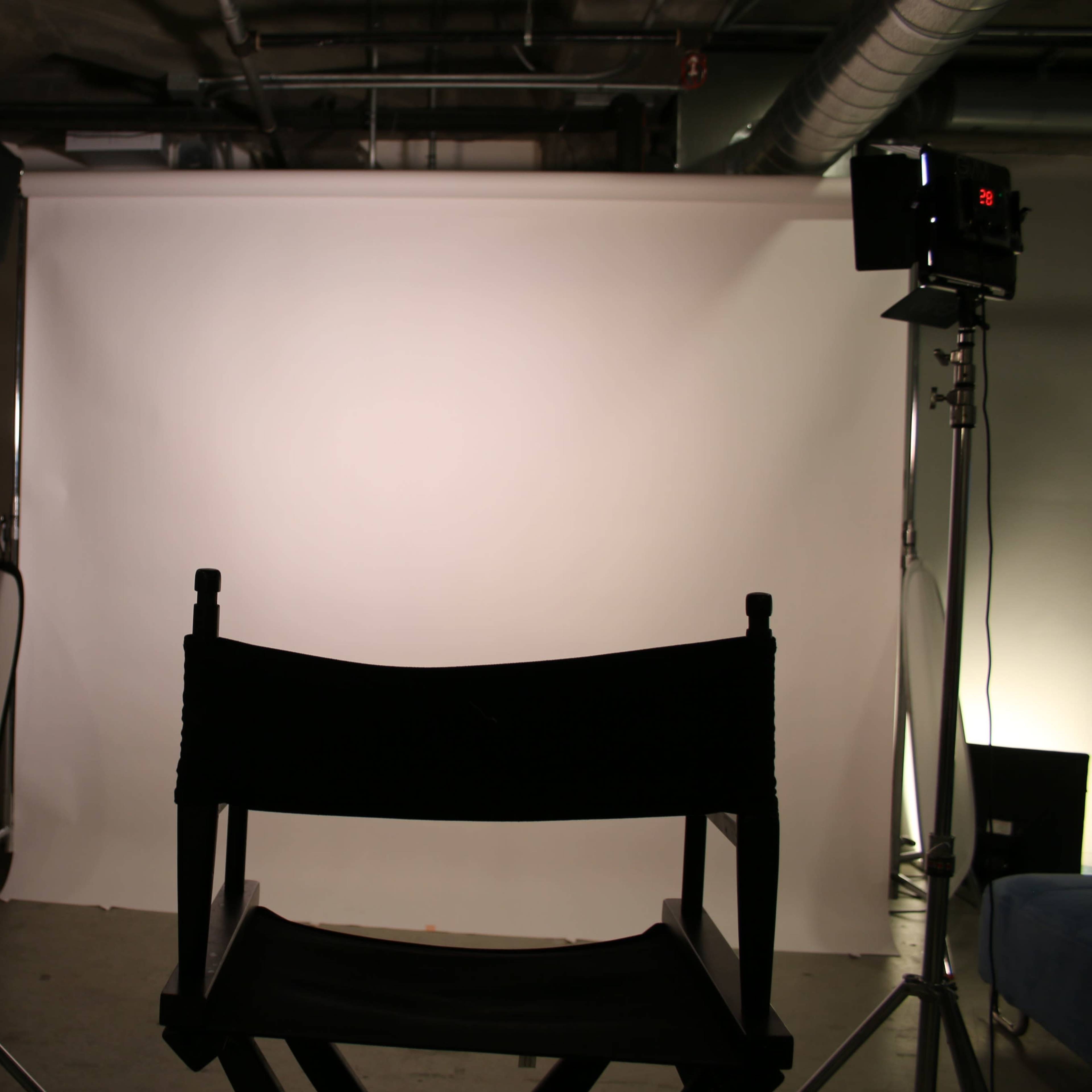 A black director's chair is positioned in front of a white backdrop with two lighting stands on either side.