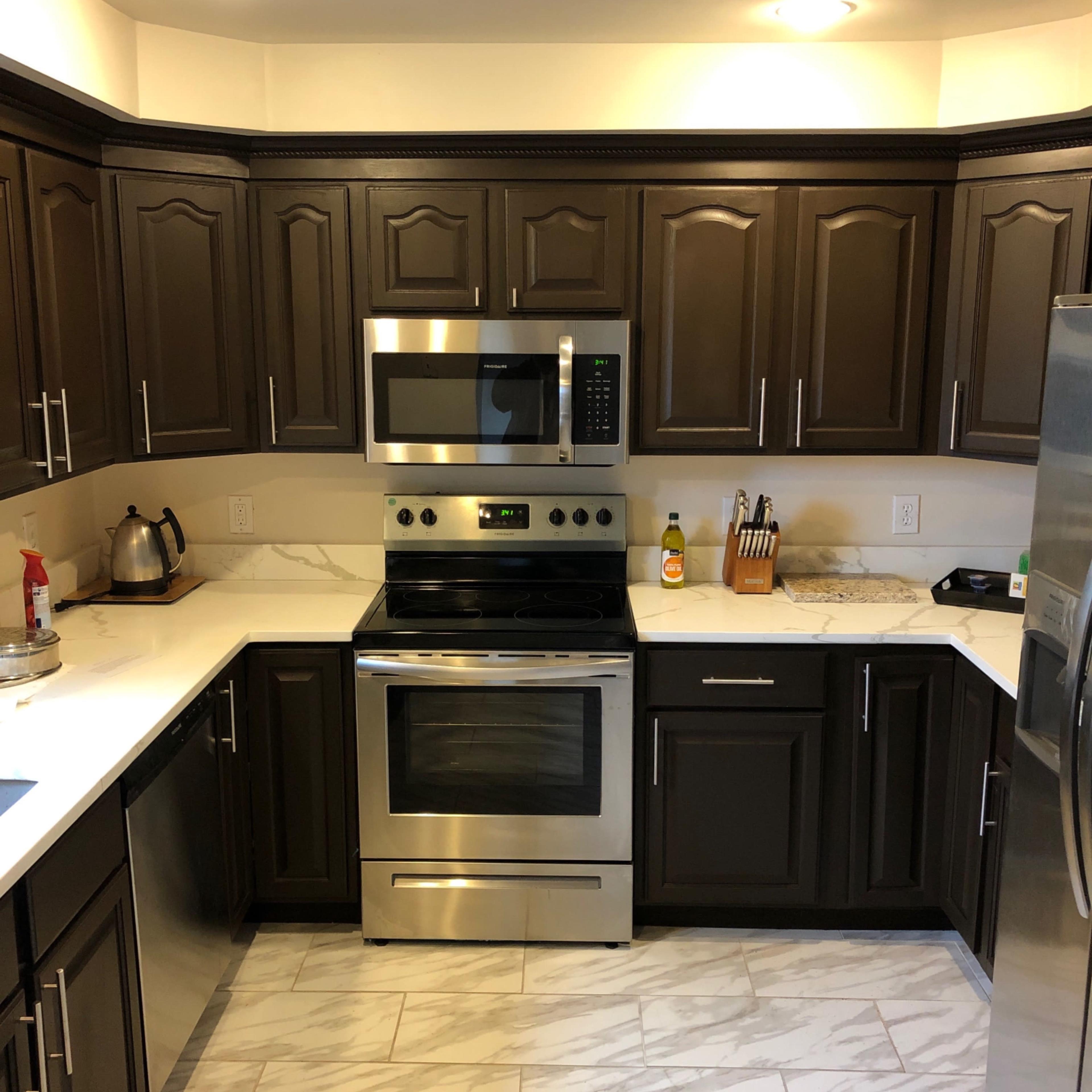 A modern kitchen with dark cabinetry, a stainless steel stove and microwave, and a marble countertop.