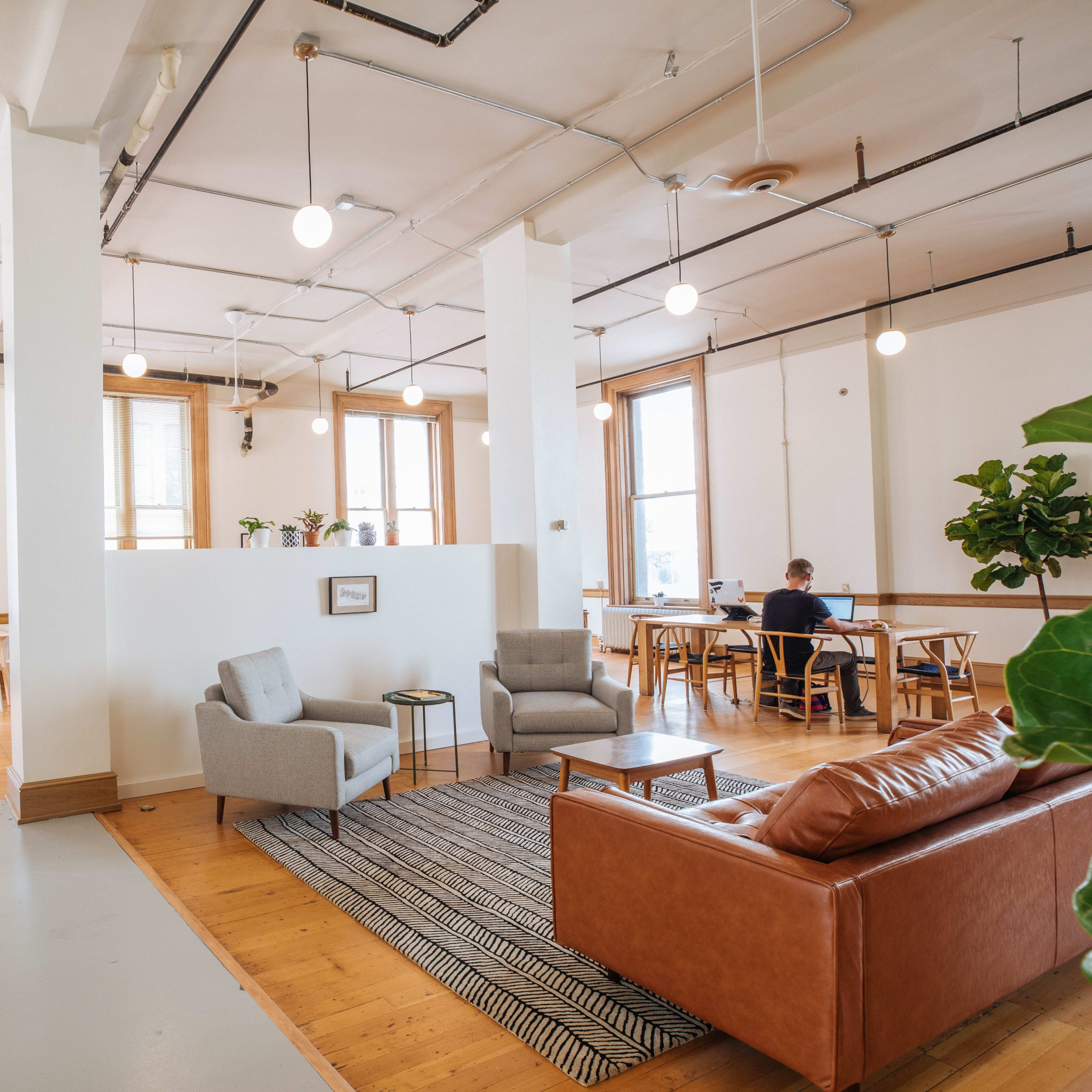 A spacious, modern office area with seating arrangements, plants, and natural light coming through large windows.