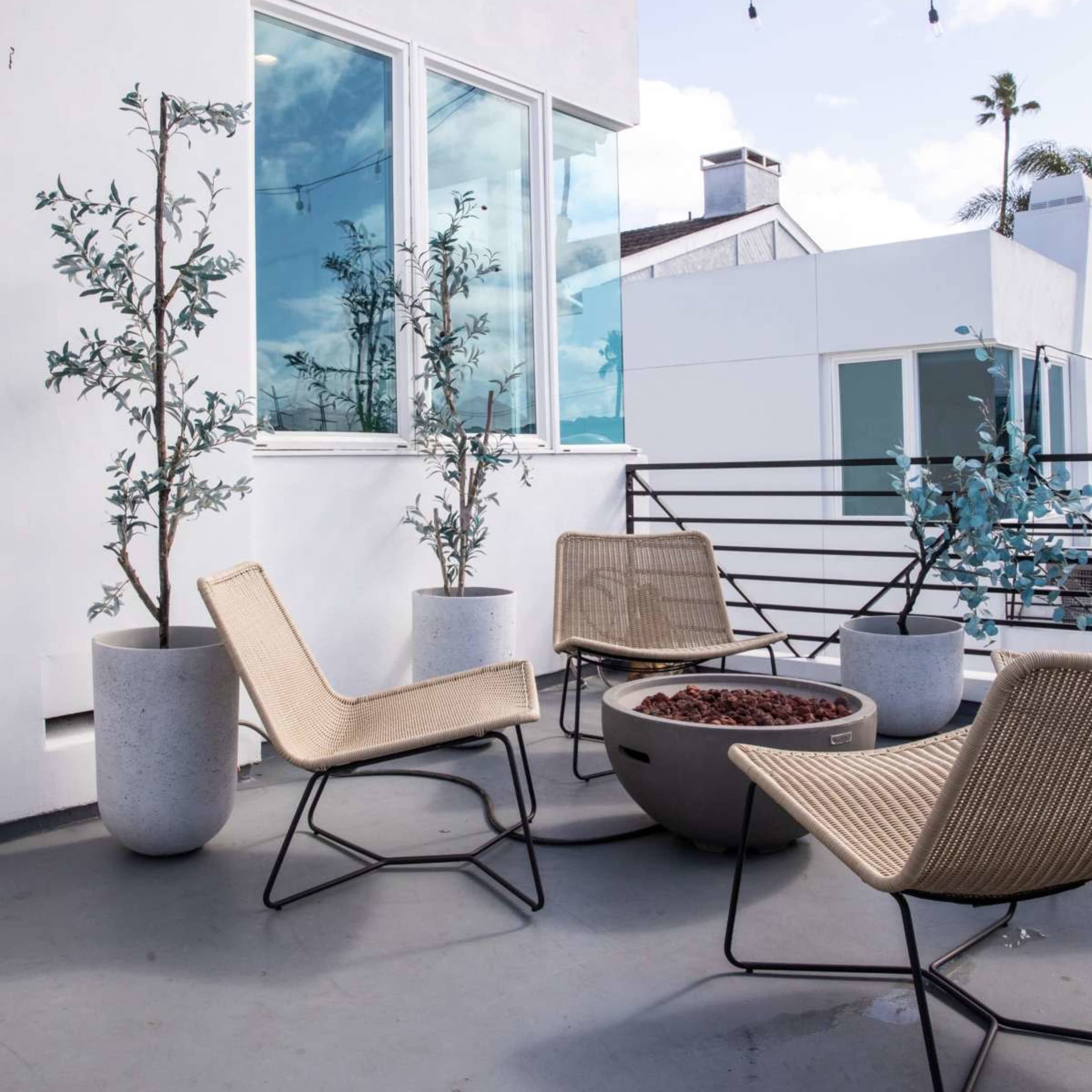 A rooftop patio features modern chairs and potted plants with a view of the surrounding buildings and sky.