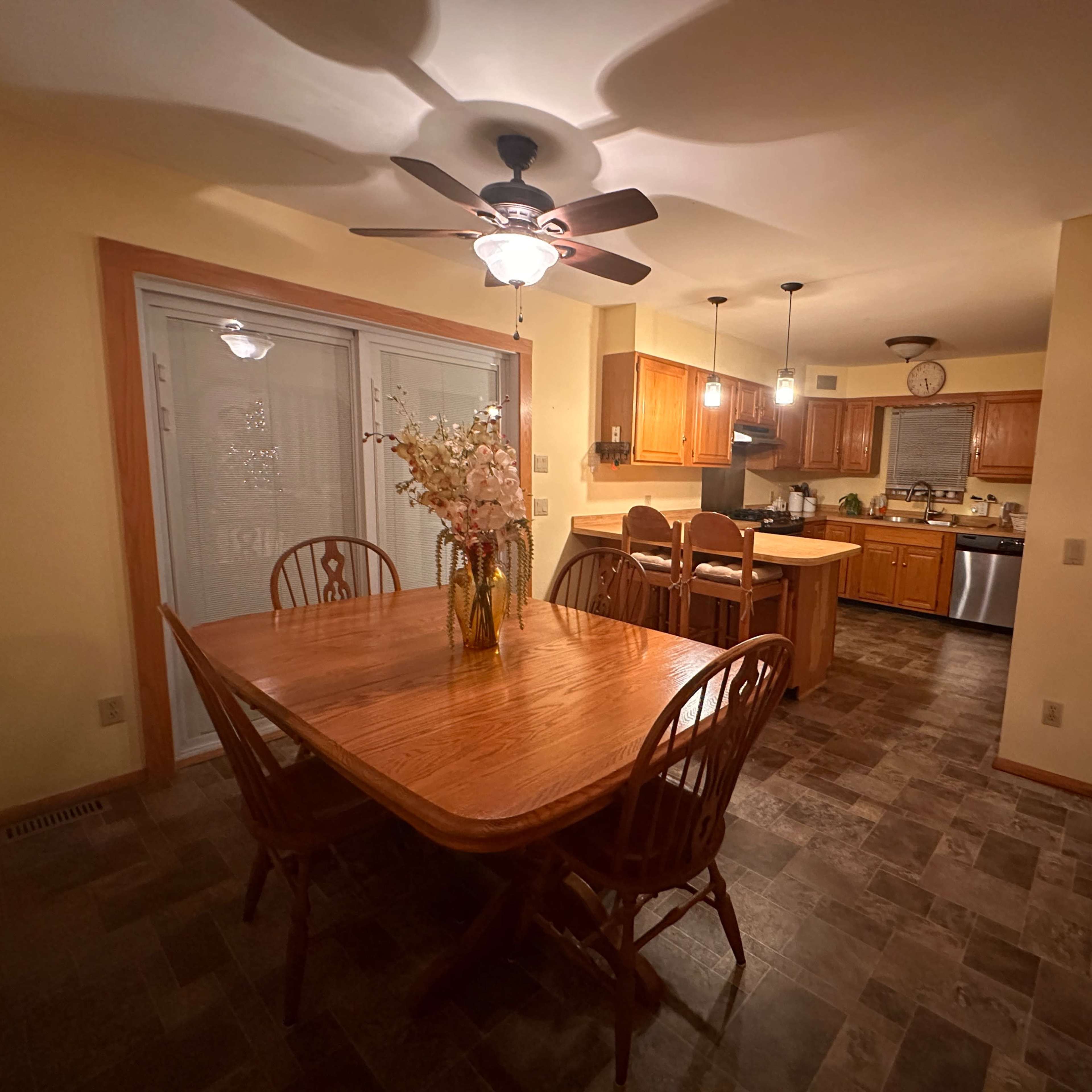 A dining area with a wooden table and chairs, adjacent to a kitchen with wooden cabinetry and modern appliances.