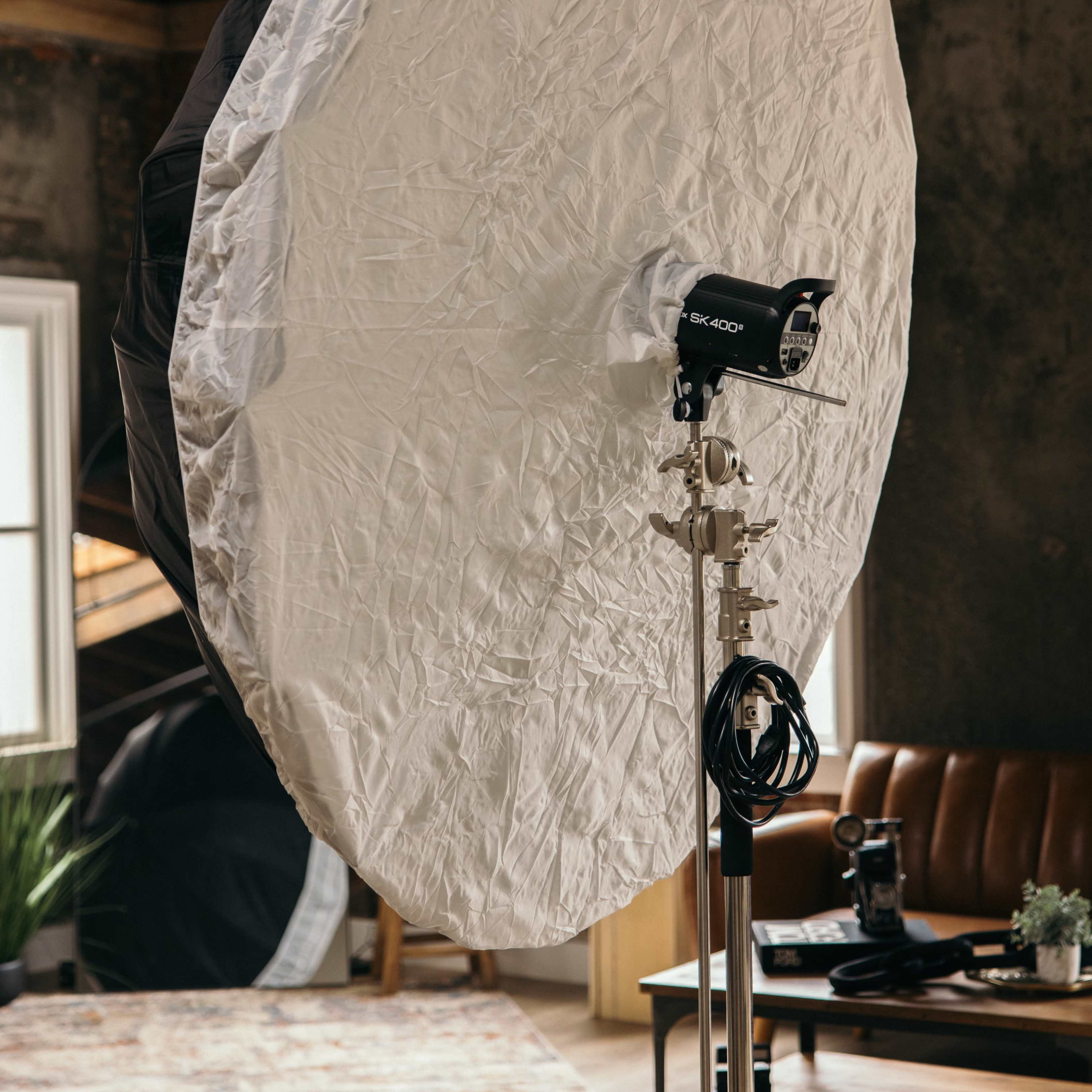 A large, circular softbox is positioned on a stand in a room with wooden floors and a brown leather couch.