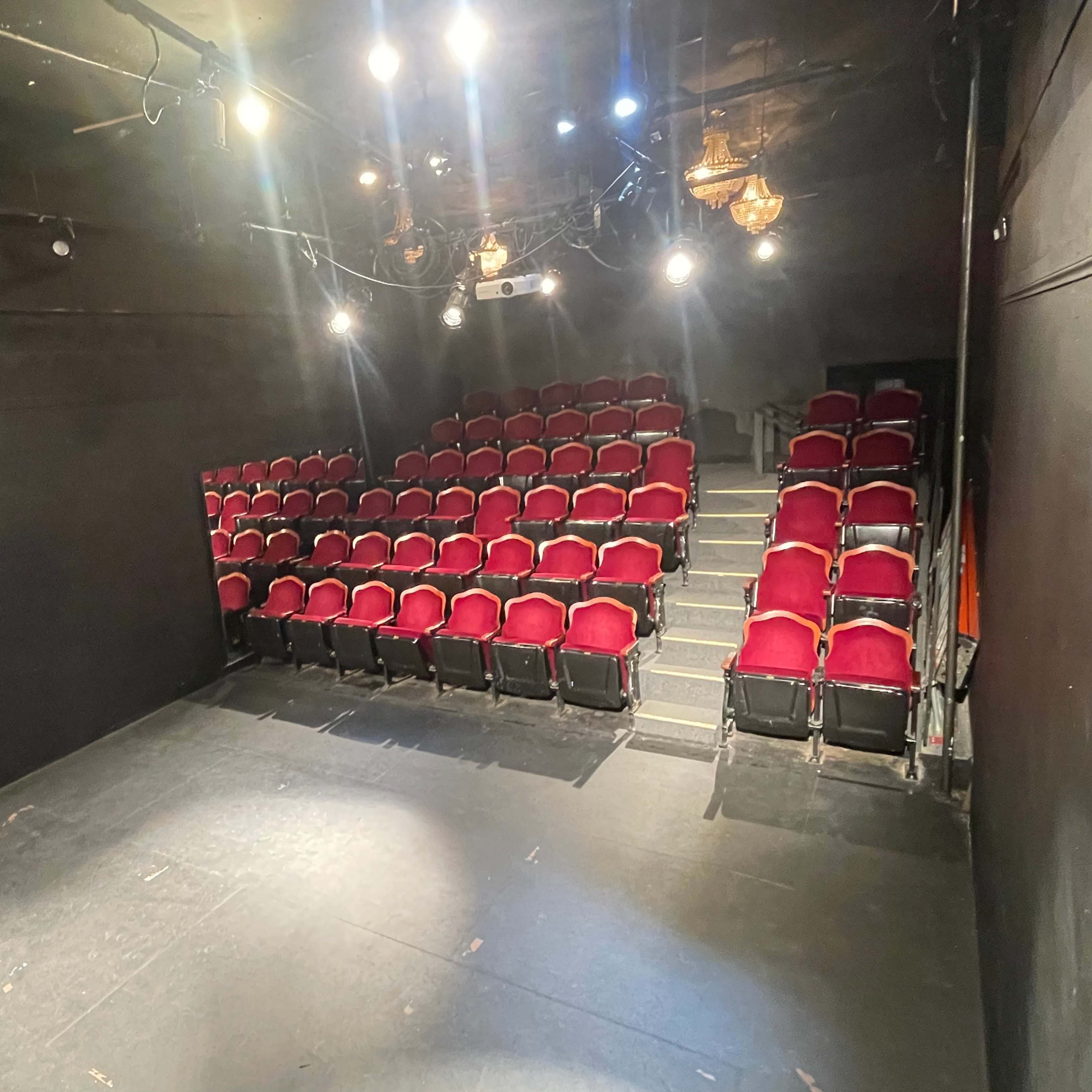 A small theater stage with red seating arranged in tiers, illuminated by overhead lights.