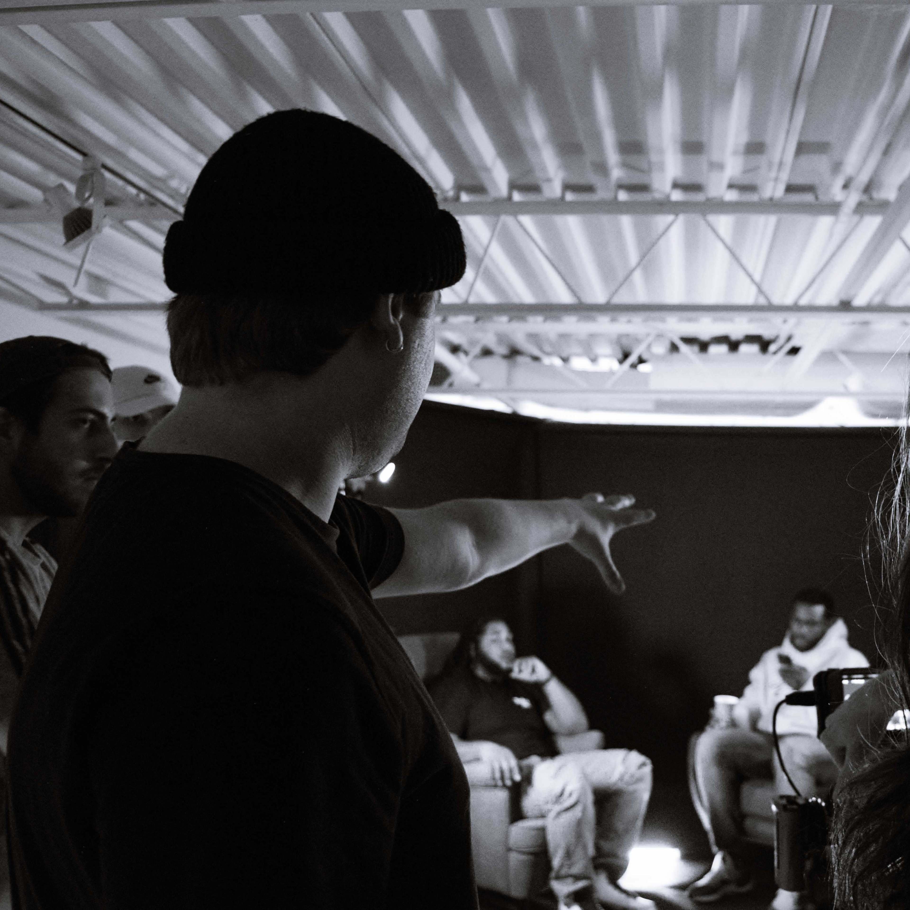 A group of people is gathered in a room, with one person gesturing towards others seated on a couch in the background.