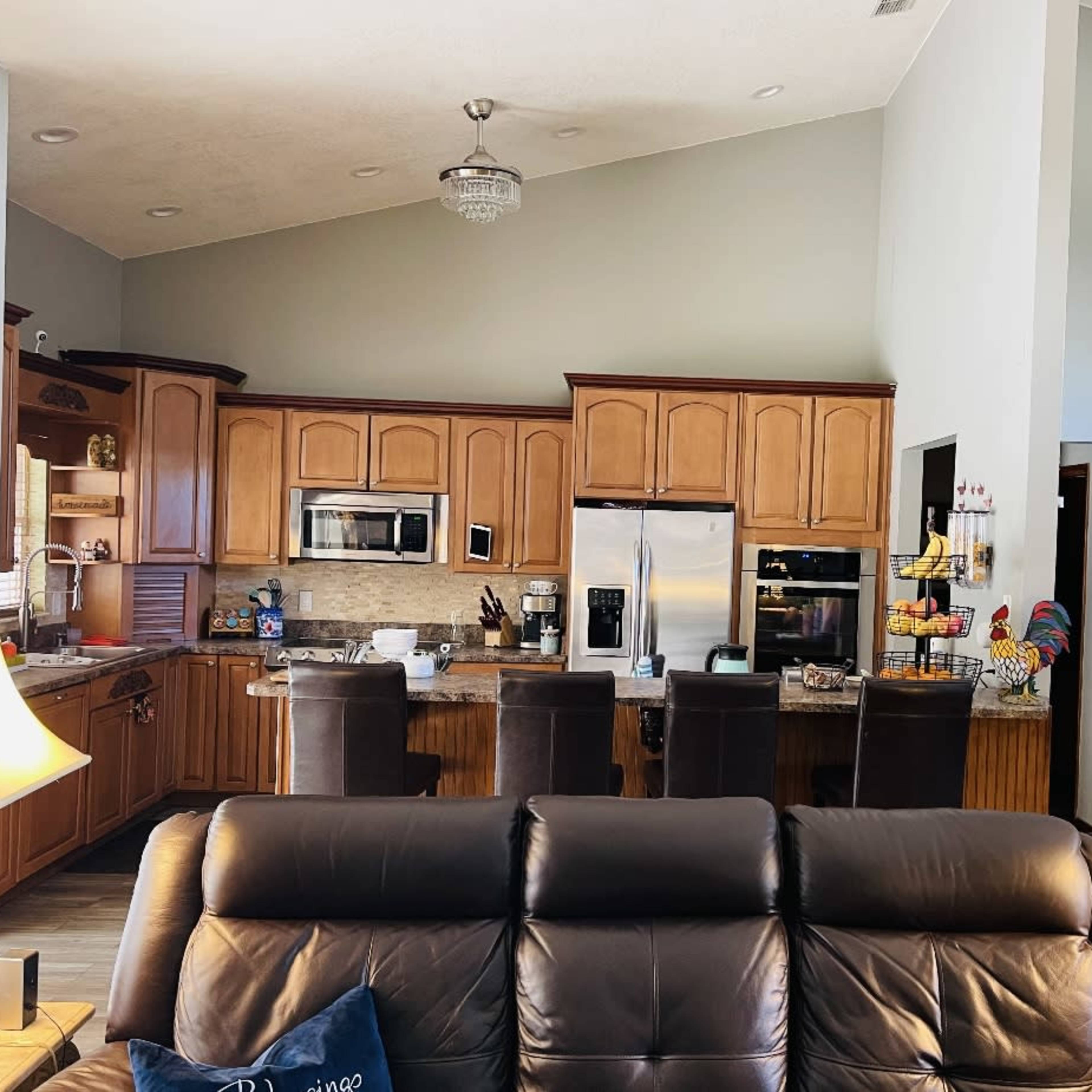 A living room with a leather sofa facing an open kitchen featuring wooden cabinets and modern appliances.