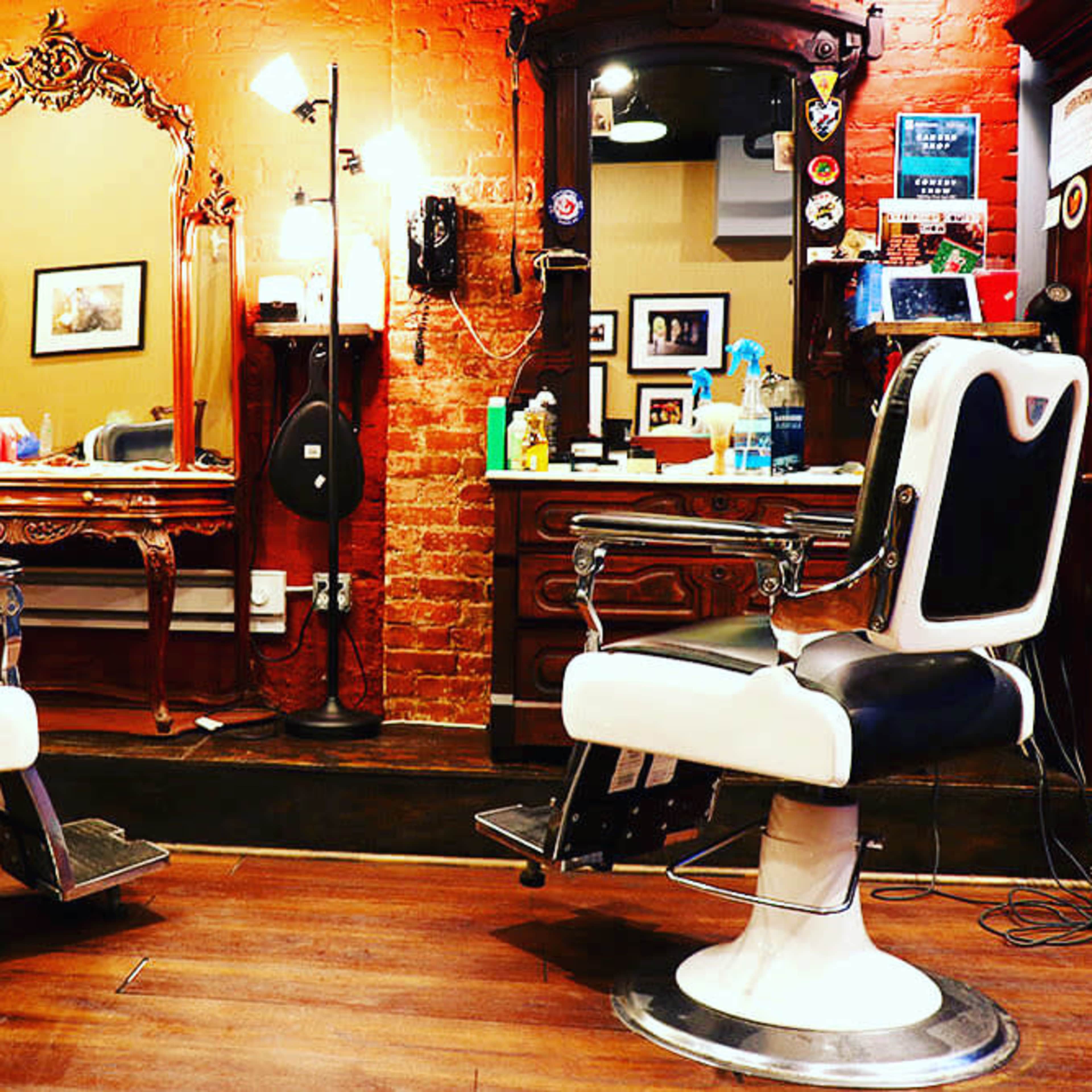 A vintage barber shop interior featuring two black and white barber chairs, ornate mirrors, and brick walls.