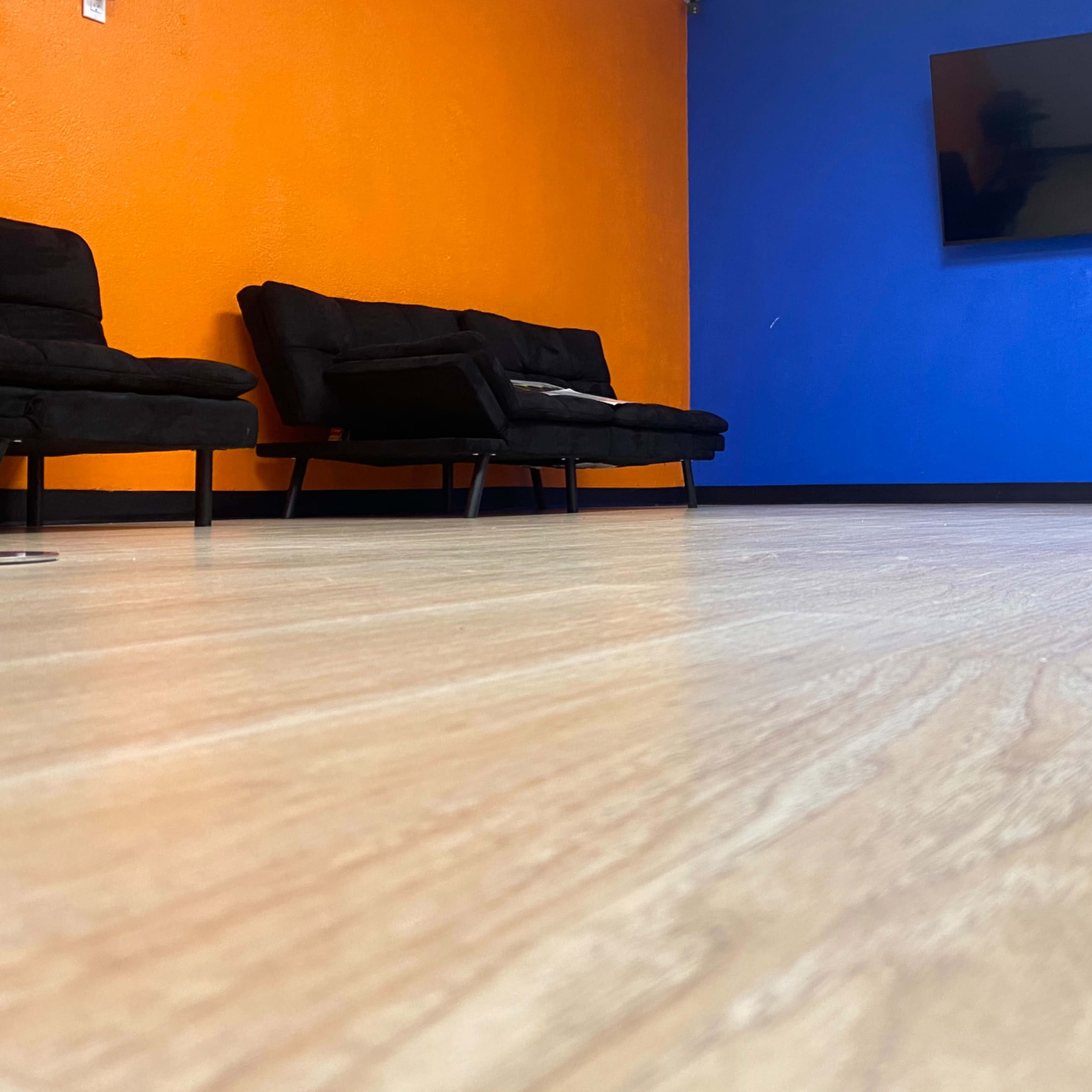 A room with an orange and blue wall, two black couches, and a wall-mounted television.