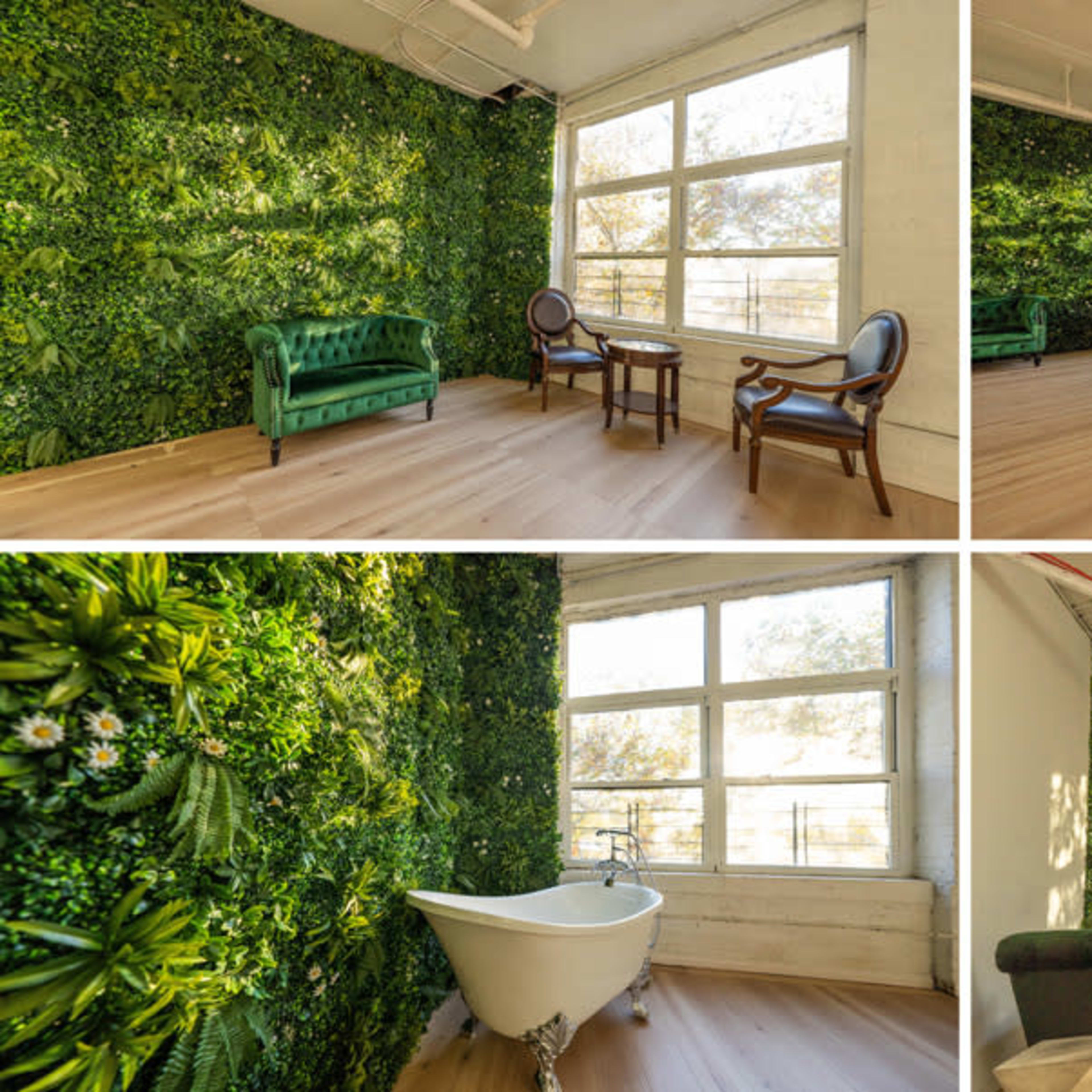 A bright room with greenery-covered walls, two chairs, a small table, and a freestanding bathtub.