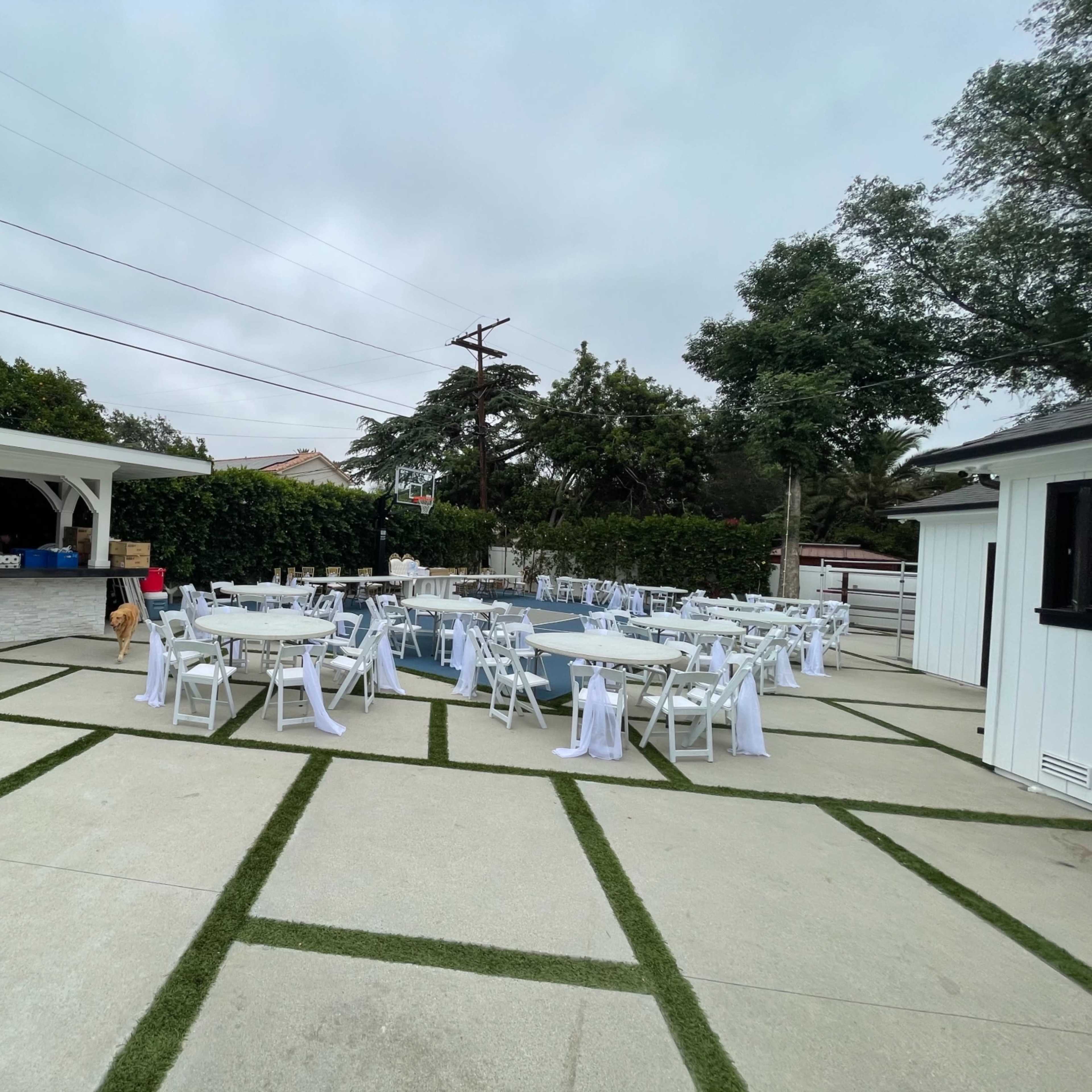 The scene shows a poolside area set up for an event, featuring several tables with white tablecloths and chairs arranged on a concrete surface.