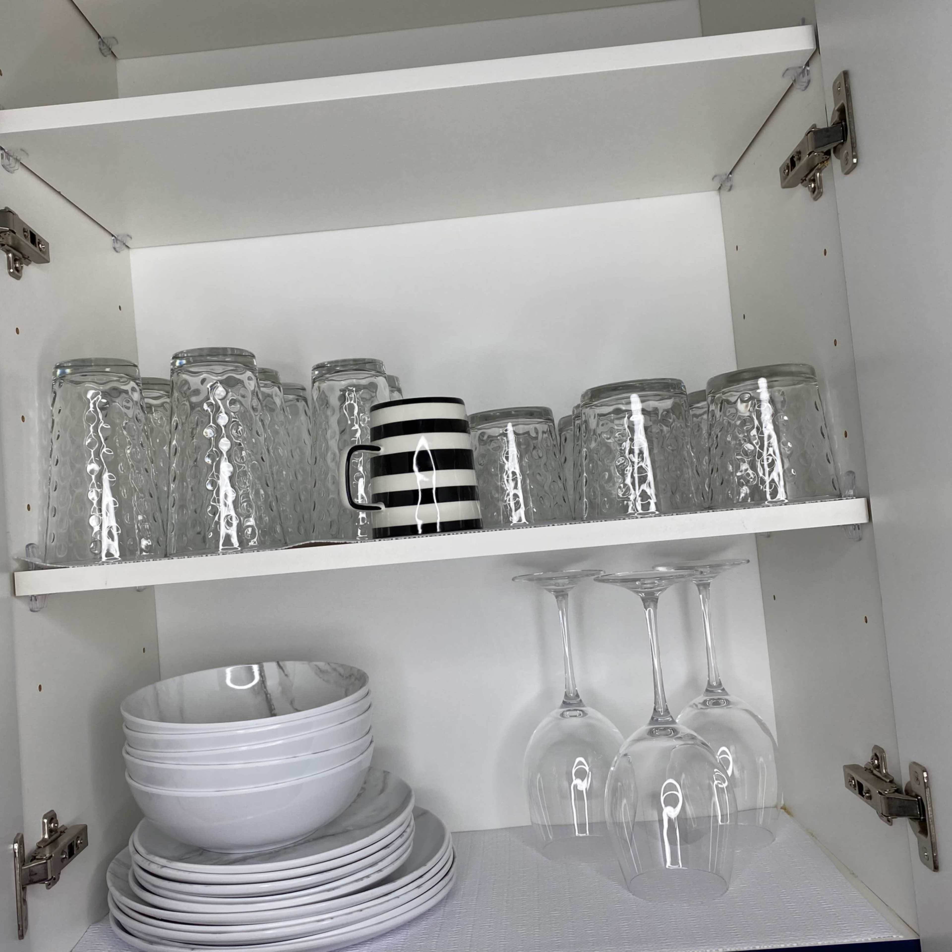 A kitchen cabinet with stacked white plates, bowls, and glasses, arranged on two shelves.